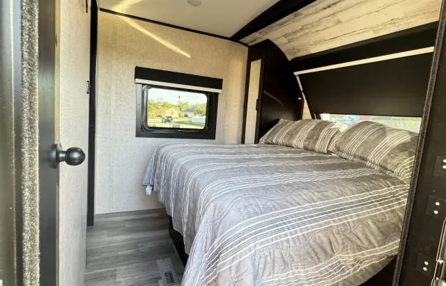 Cozy rv rental bedroom features a comfortable bed with striped linens, a window showing outside, and modern interior details.. Jayco White Hawk 2023
