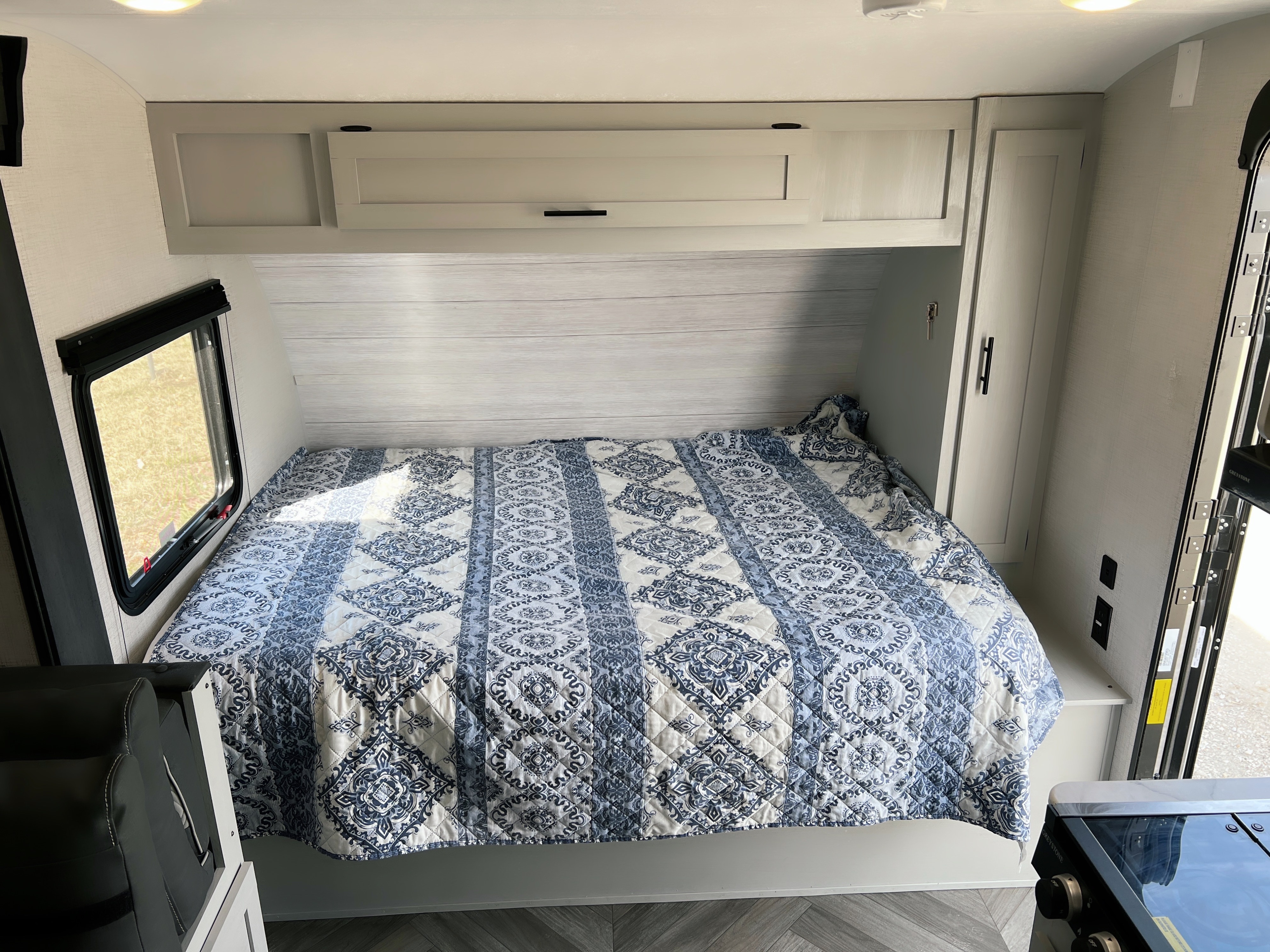 Inside a comfortable RV rental: a bedroom featuring a blue patterned quilt, overhead cabinets, and a window with outside views.. Forest River Salem FSX 2022