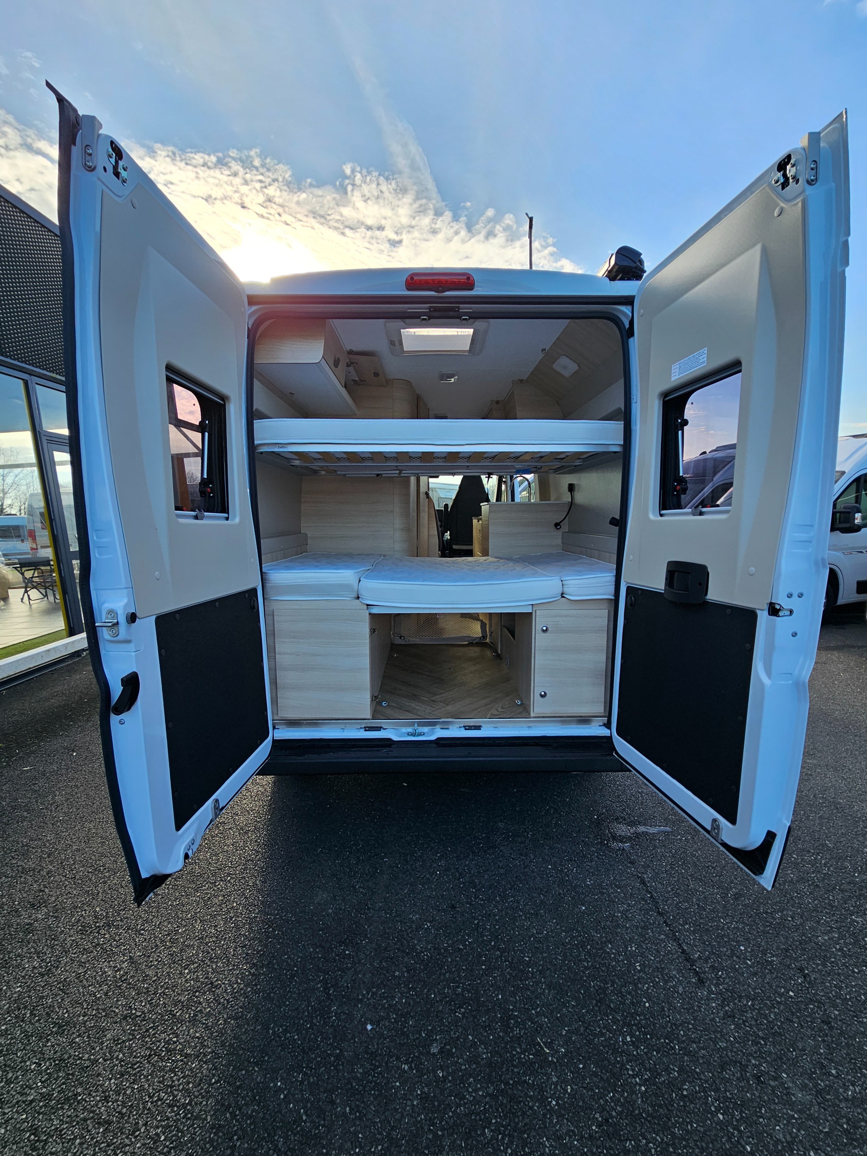 RV rental: Rear interior of a camper van with open doors, revealing light wood furnishings and stacked bunk beds.. Chausson V594 MAX 2024