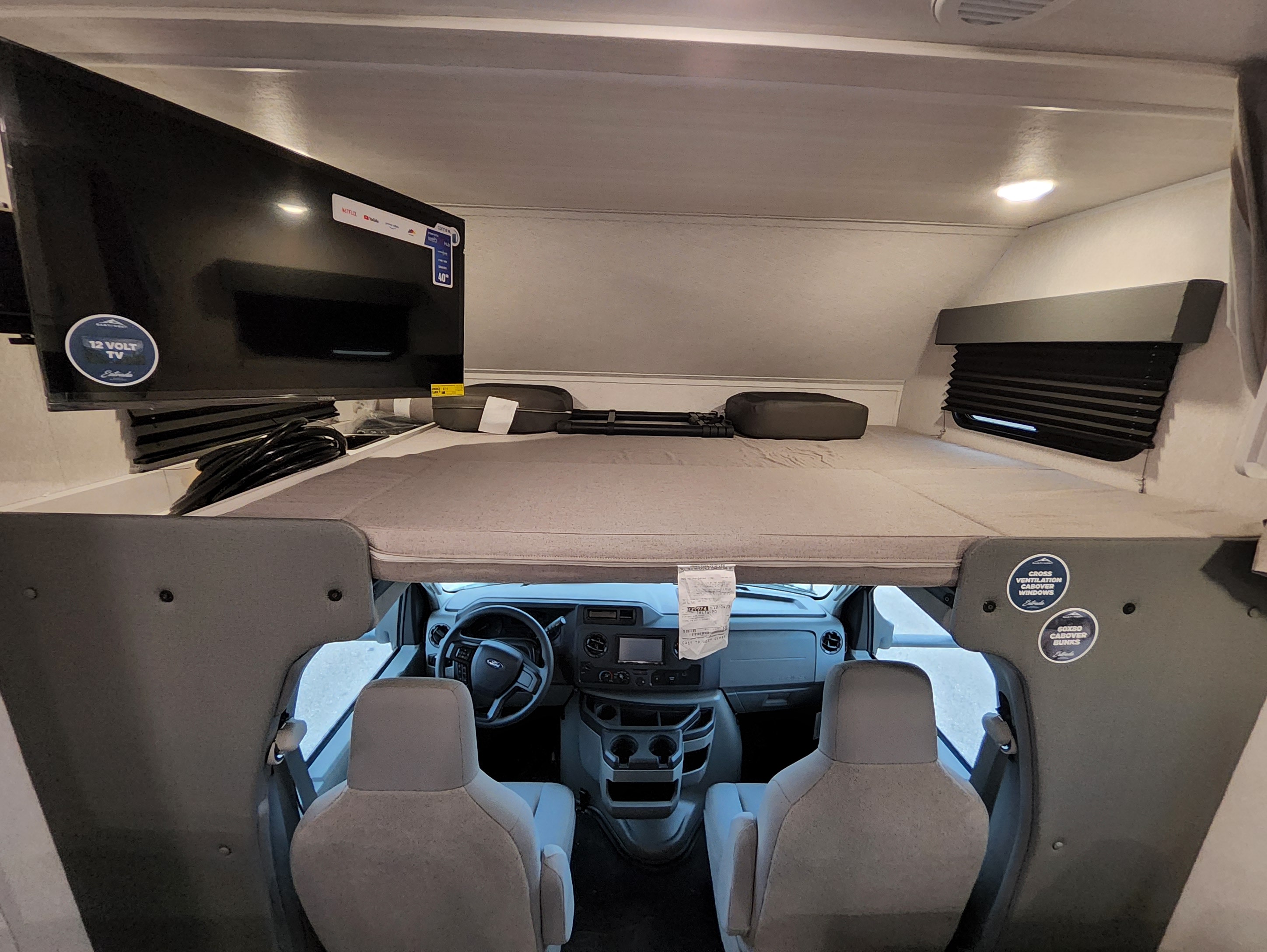 Inside an RV rental: a cozy cabover bunk bed with TV overlooks the front Ford cockpit, perfect for road trips.. East To West Entrada 2025