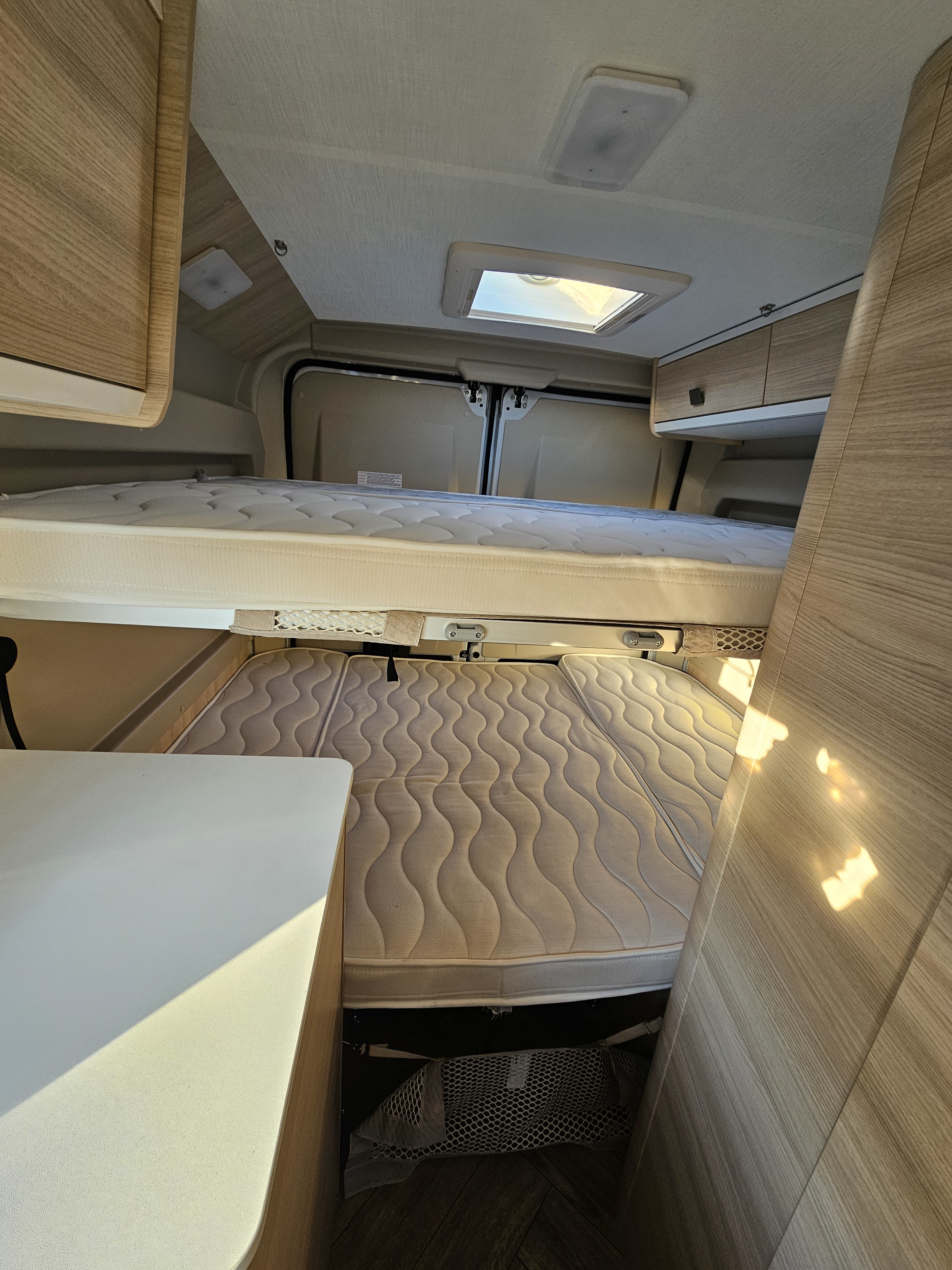 RV rental interior: upper and lower bunk beds with soft mattresses, wood accents, and a ceiling vent. Spacious sleeping area.. Chausson V594 MAX 2024