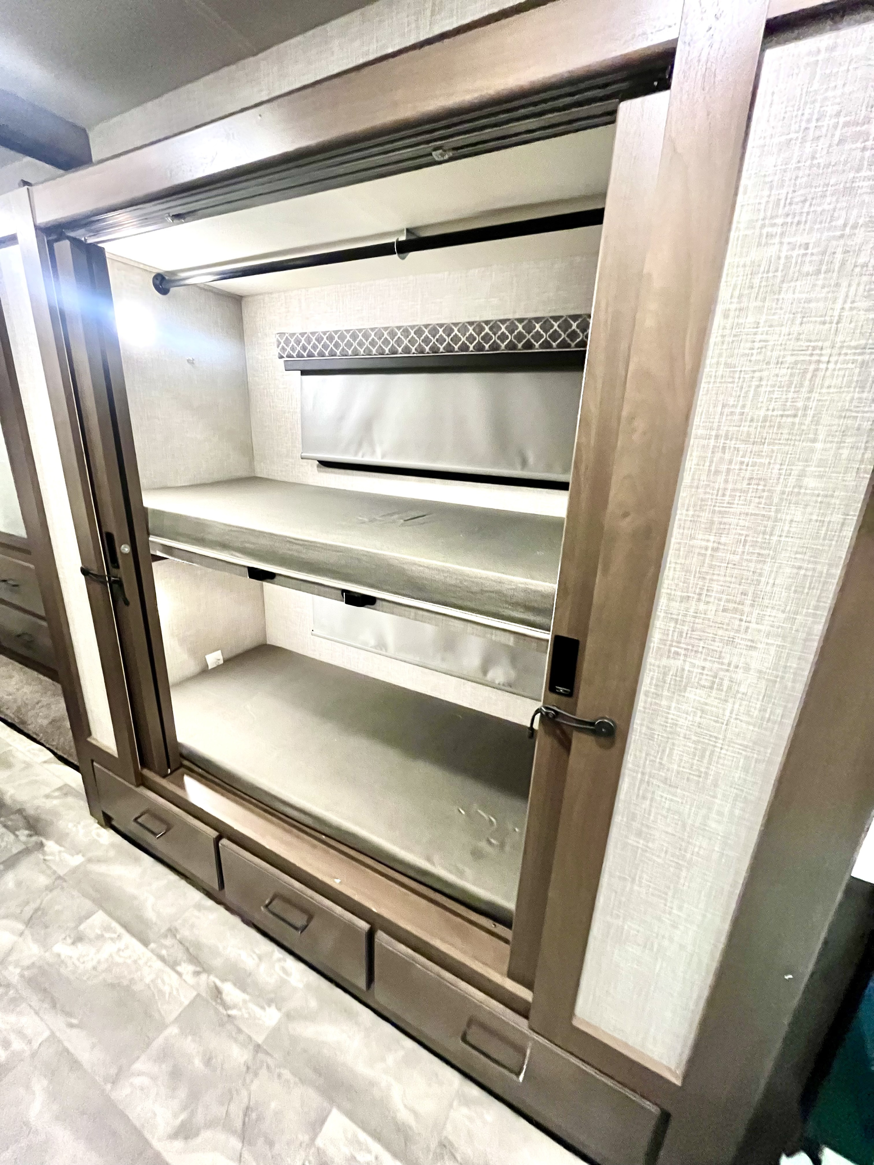 Compact RV rental bunk beds with storage drawers and a window shade, accessible via sliding doors.. Thor Windsport 2022