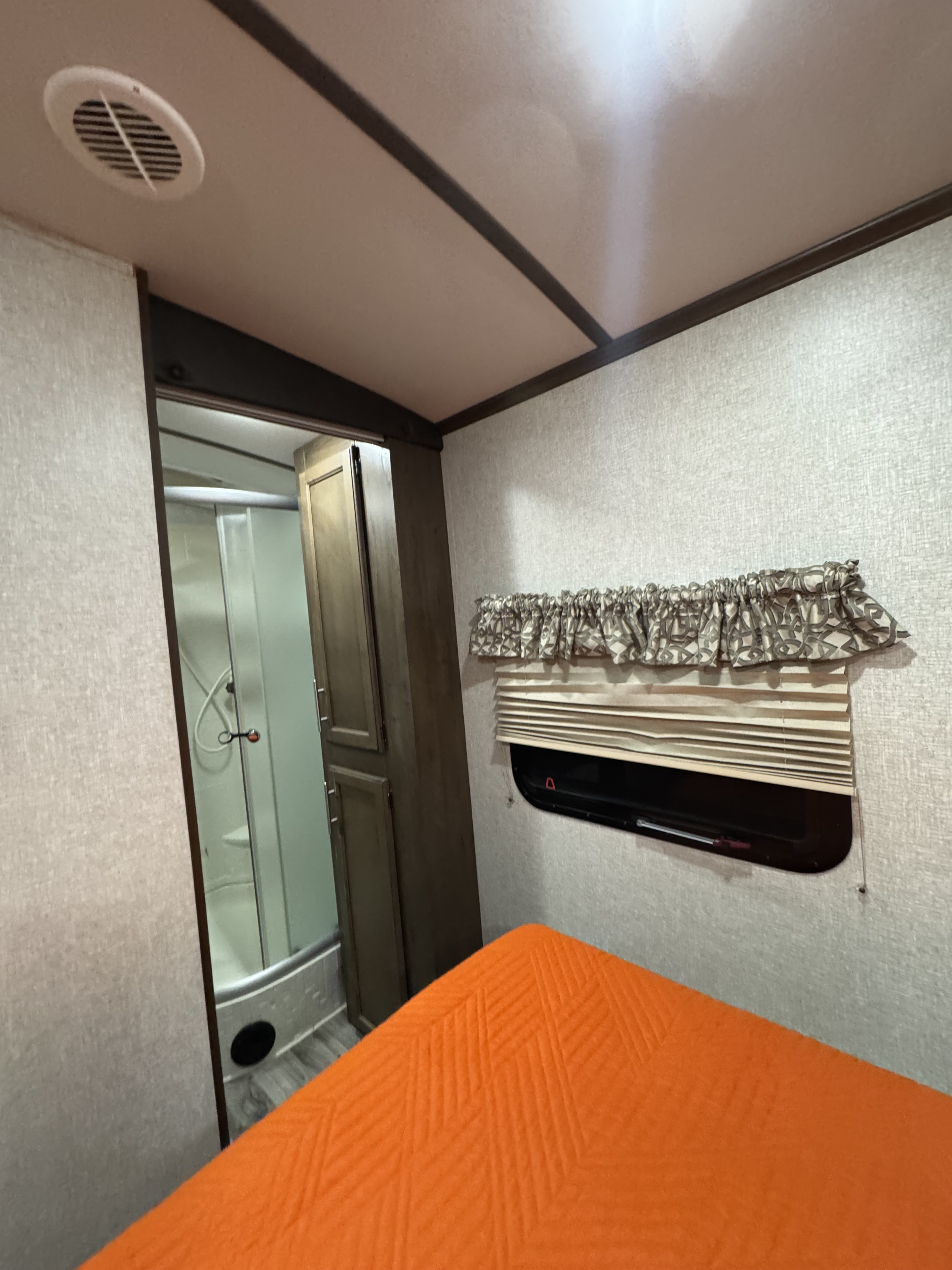RV rental interior: cozy bedroom with orange bed and window, plus compact bathroom with shower stall.. Keystone RV Cougar 2019
