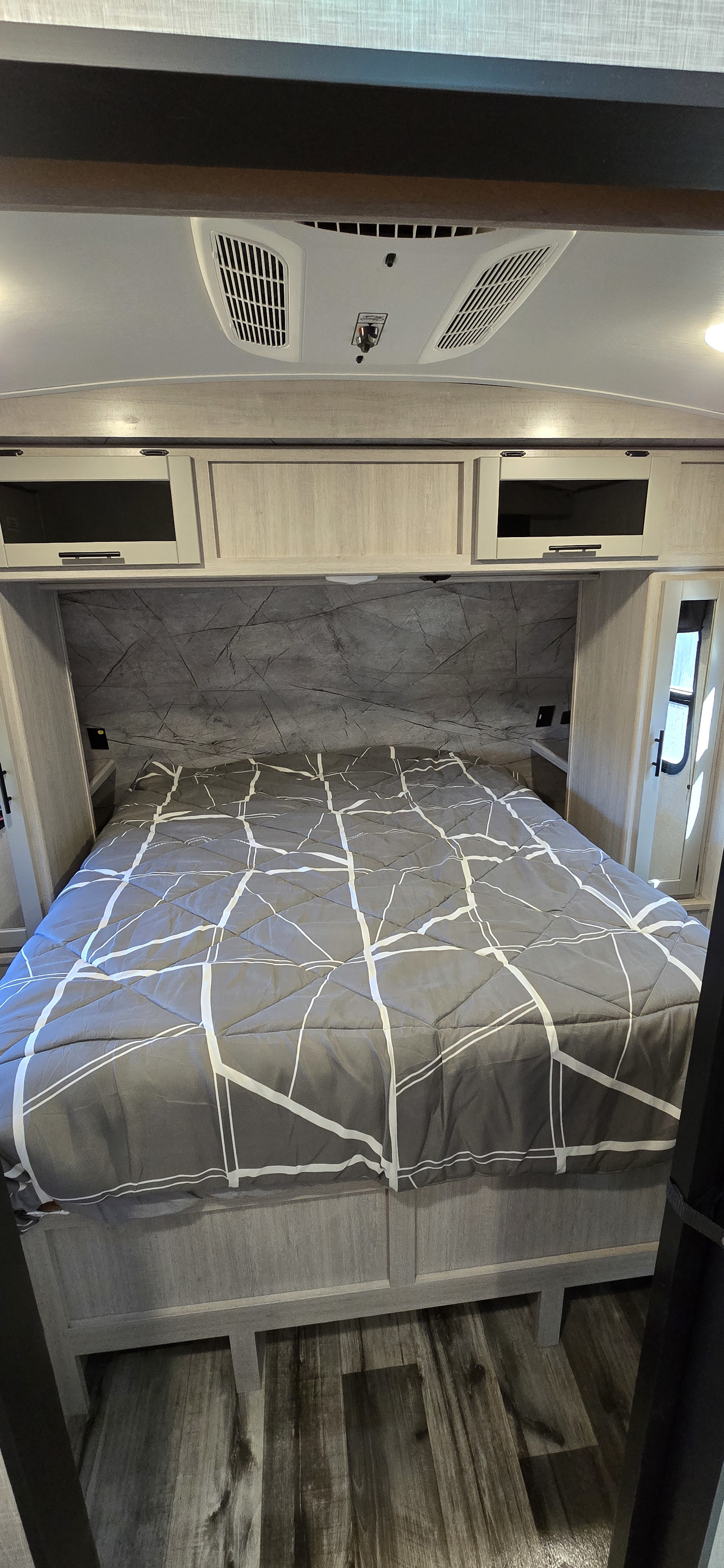Cozy RV rental bedroom featuring a large bed, overhead cabinets, and an AC unit for comfort.. Crossroads RV Sunset Trail Super Lite 2023