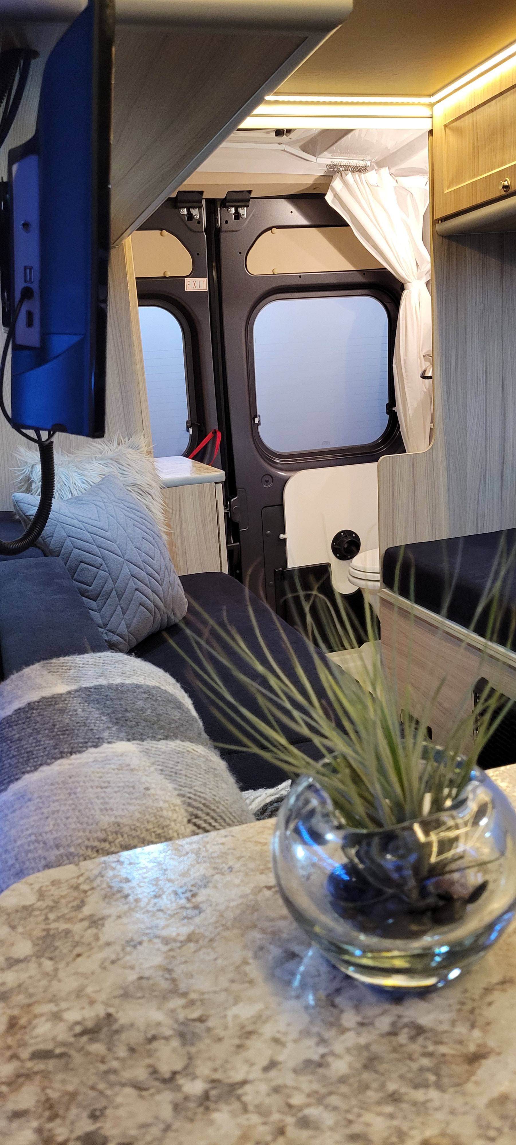 Inside a comfy RV rental: view of bed, TV, rear "EXIT" doors, and a shower area. Perfect for van life adventures.. Sunlight Sunlight Class B 2018