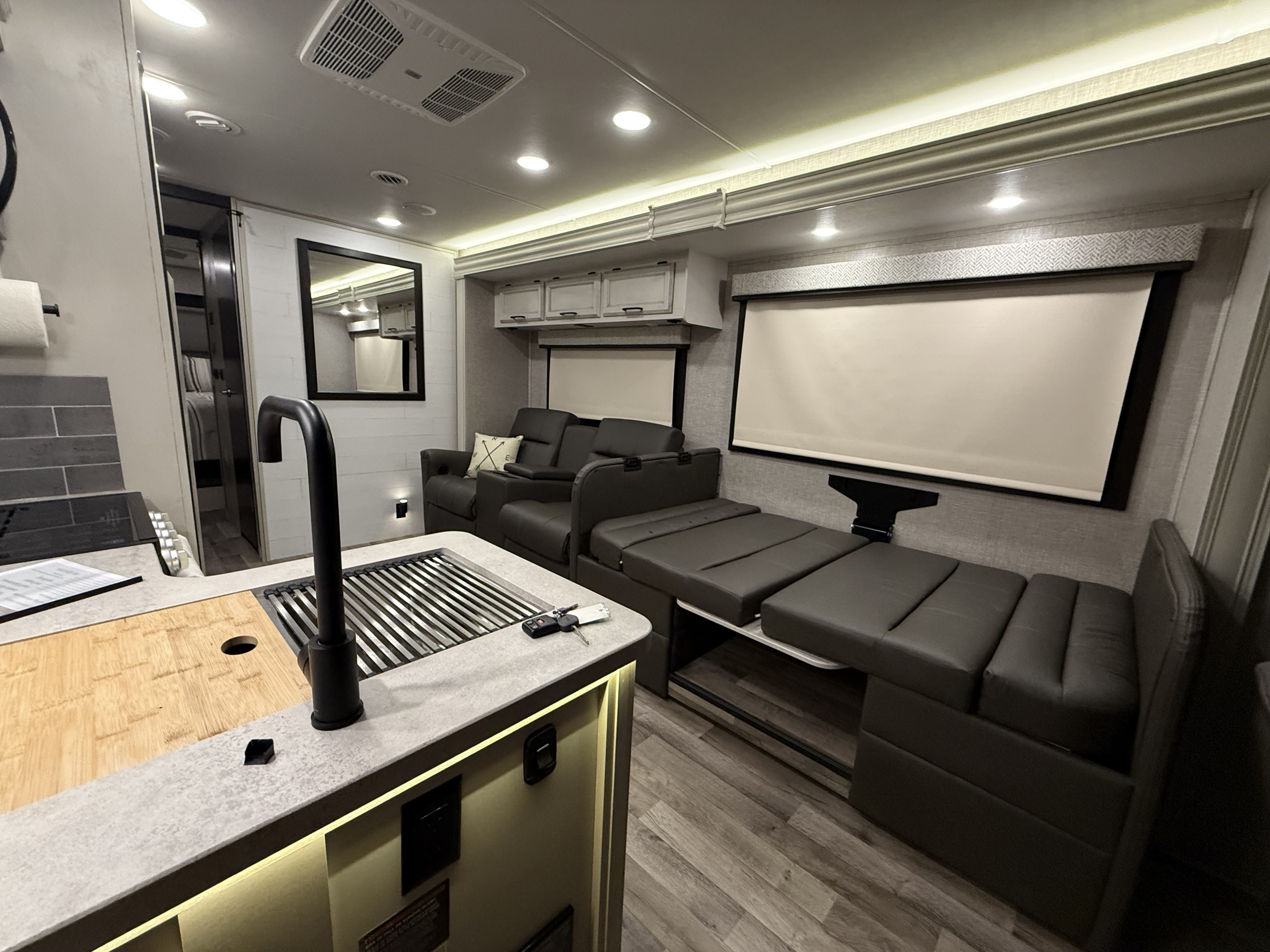 Spacious RV rental interior featuring a modern kitchen island, dark leather seating converting to a bed, and bright lighting.. Jayco Greyhawk 2023
