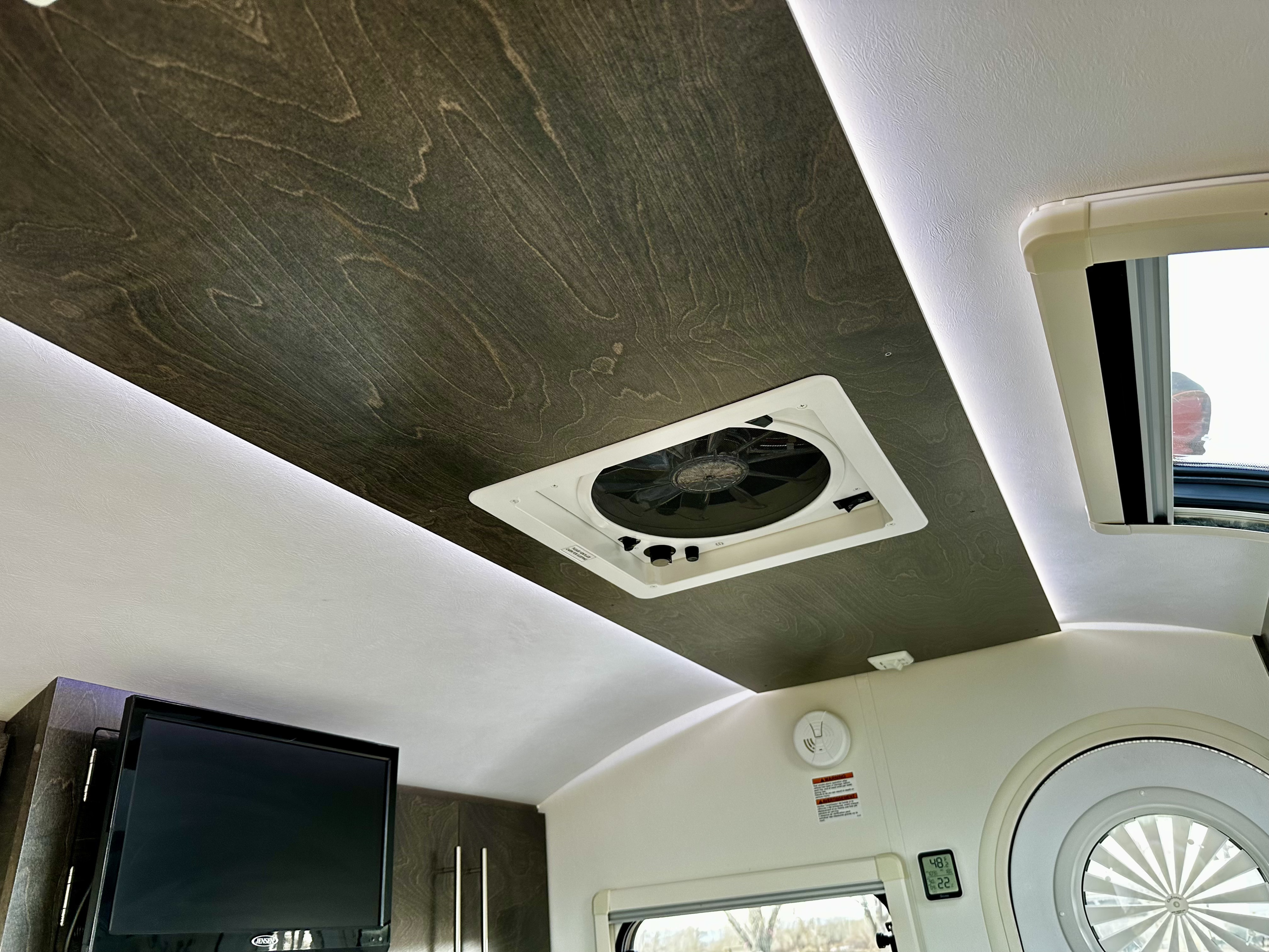 Modern RV rental interior: dark wood ceiling with vent, ambient lighting, TV, and climate display for comfortable travel.. nuCamp T@G 2020