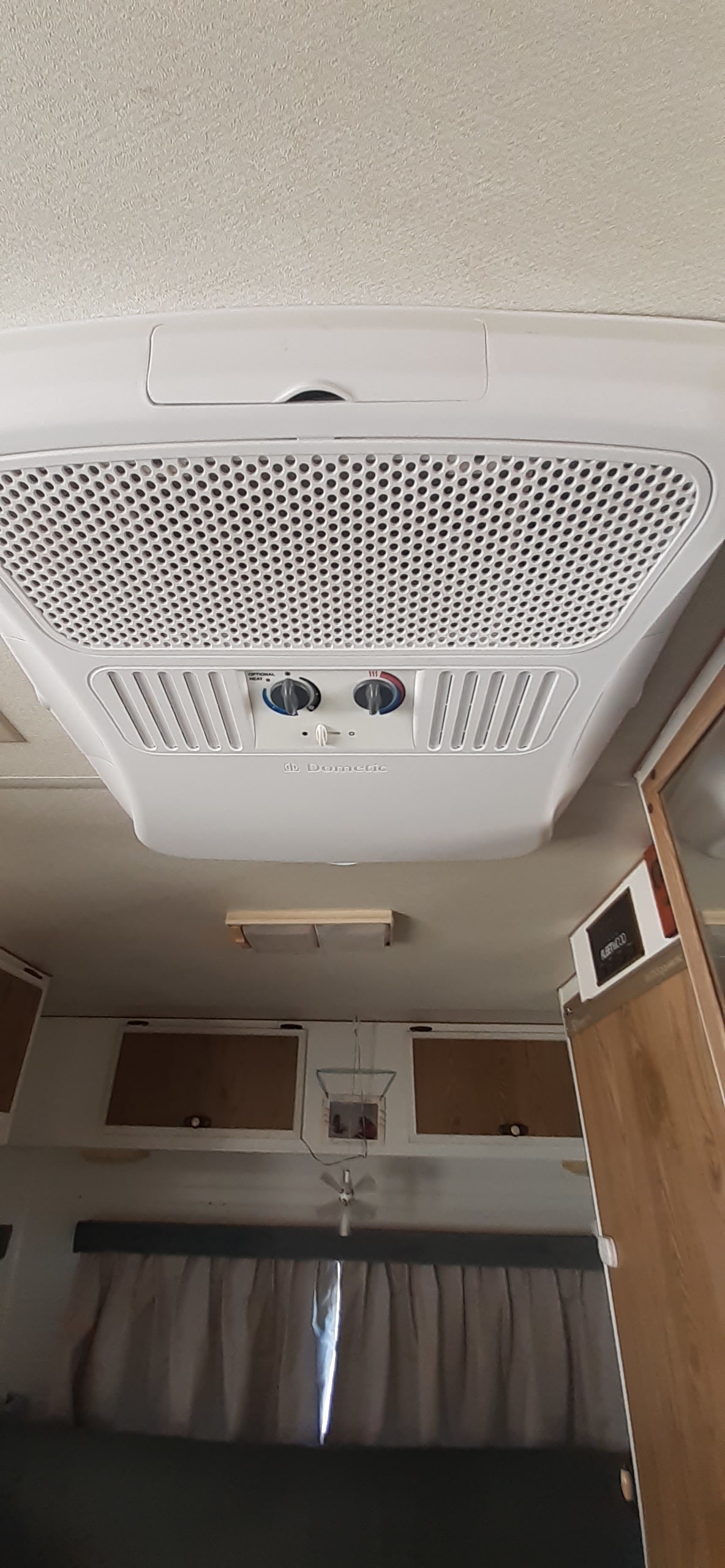 View of a Dometic RV air conditioner mounted on the ceiling of an rv rental, with visible controls and cabinetry.. Fleetwood Prowler 1988