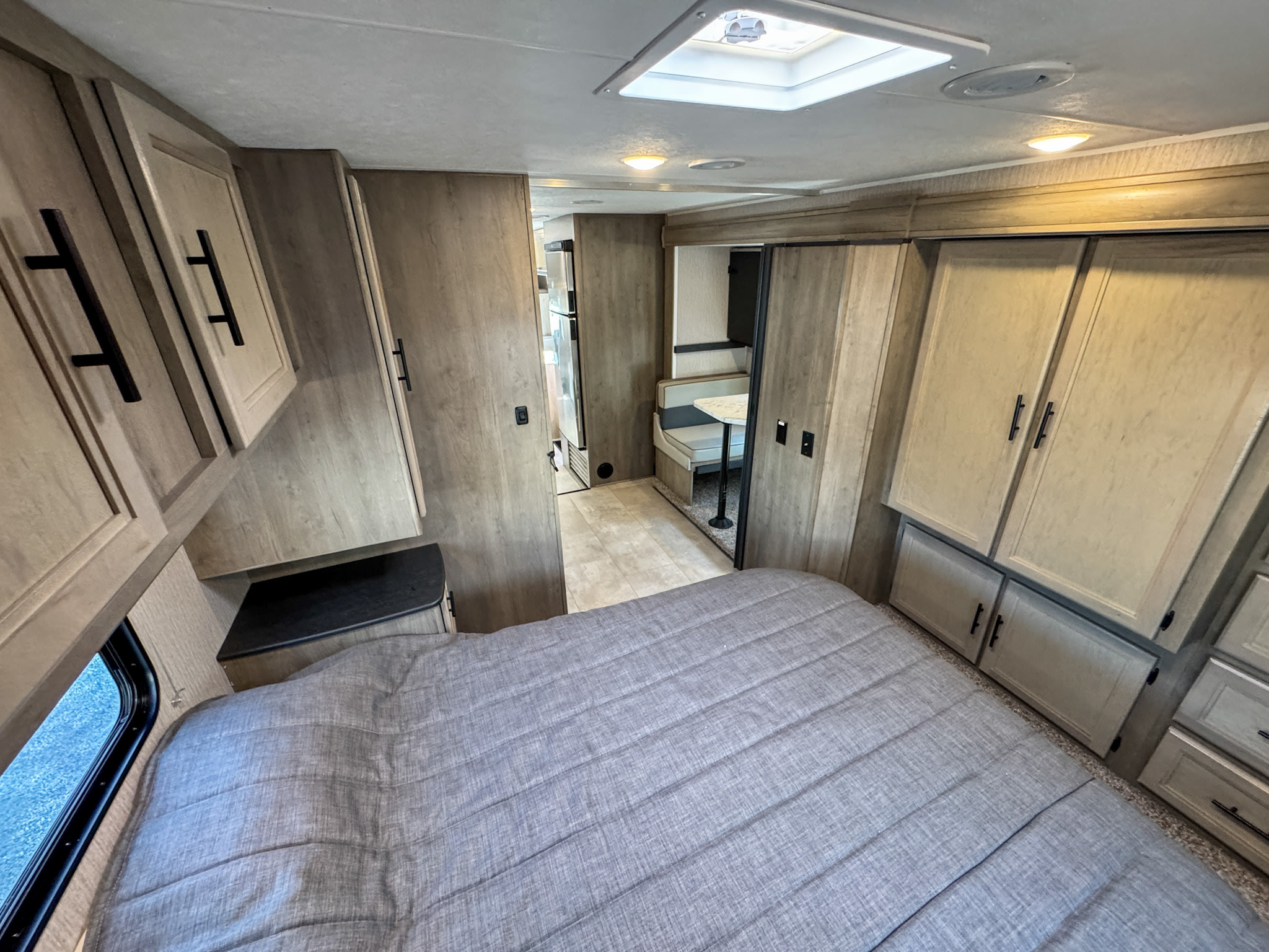 RV rental interior: a comfy bedroom with light wood cabinets, leading to a functional dinette and kitchen area.. Coachmen Freelander 2023