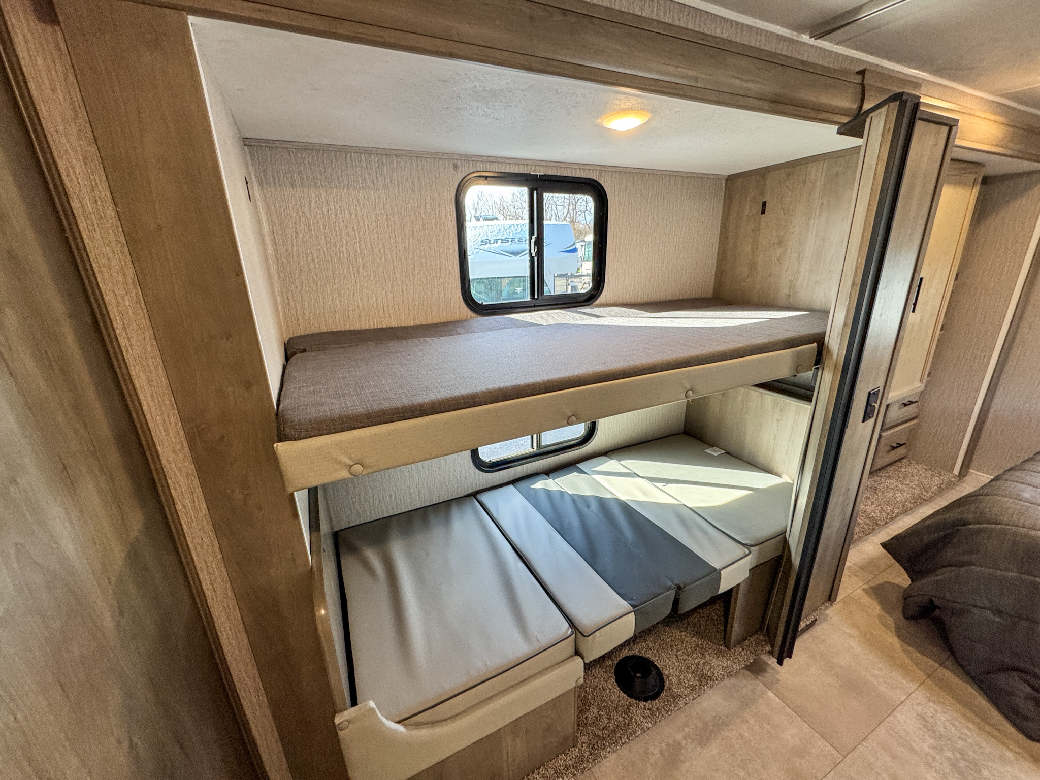 Explore this RV rental's clever bunk beds! A top bunk with a window and a versatile lower lounge are perfect for travel trailer adventures.. Coachmen Freelander 2023