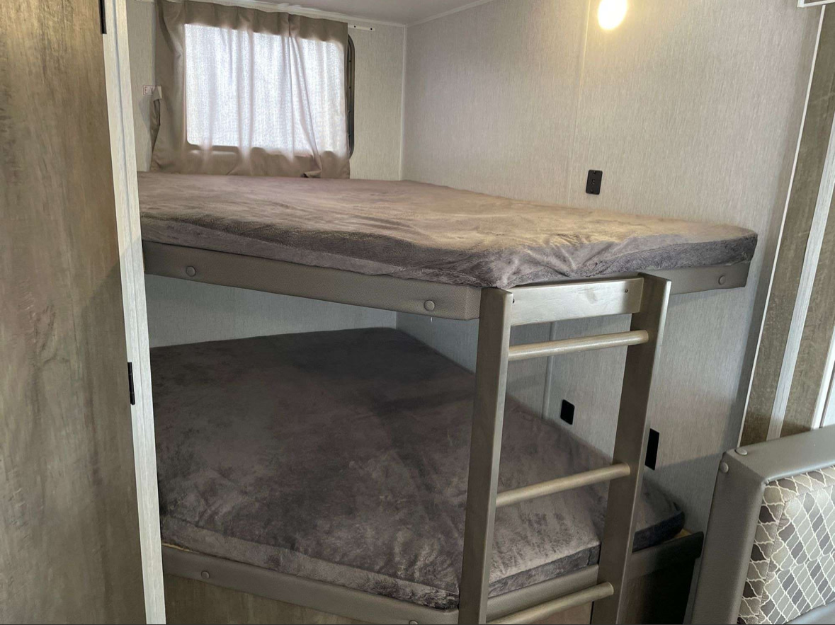Bunk beds in a modern RV rental, featuring cozy gray bedding & ladder access. Ideal for family trips.. Forest River Evo T2400BHXW 2022