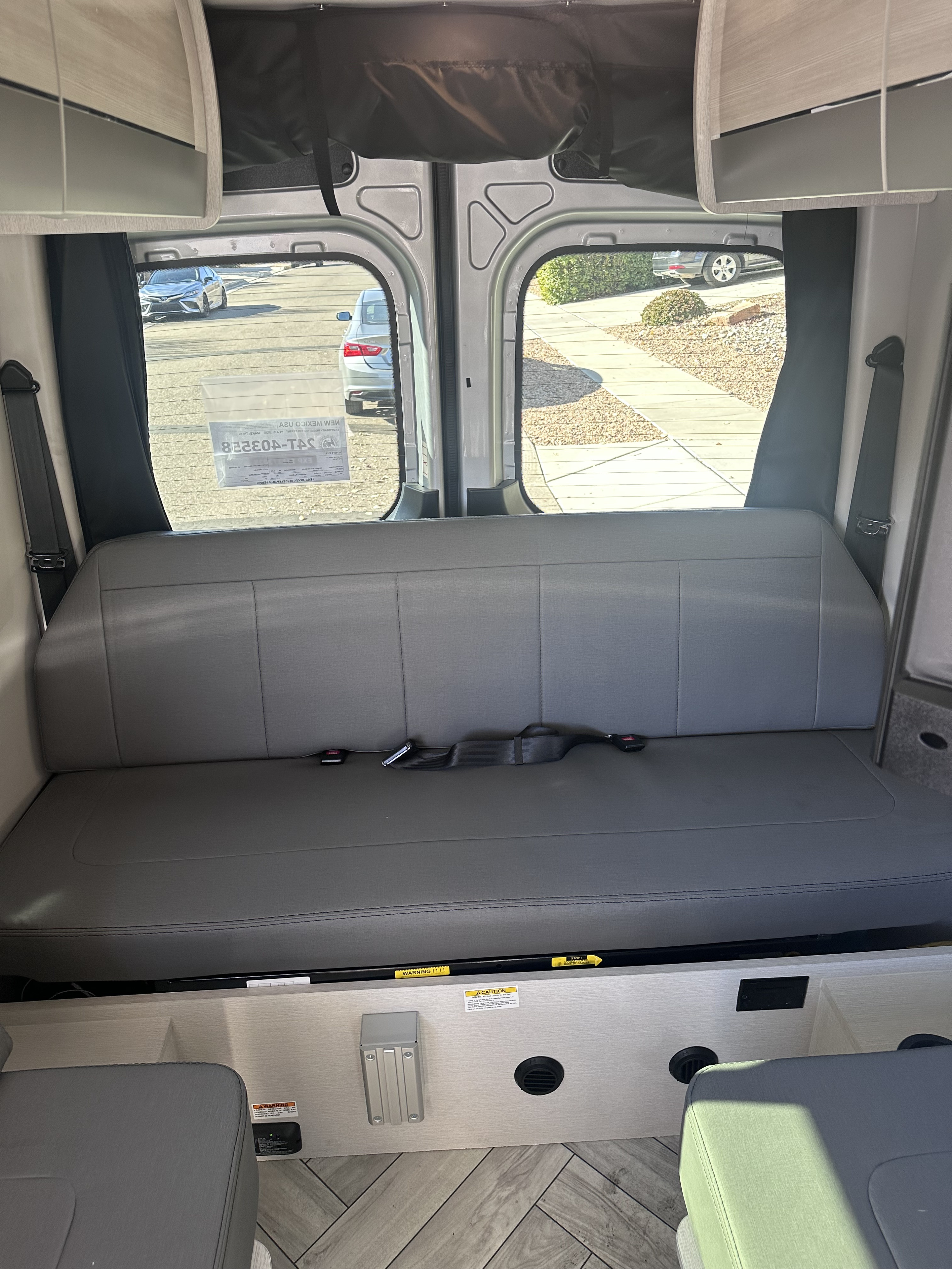 Inside an RV rental: Spacious rear interior featuring a gray bench seat with seatbelts, ample storage, and large windows.. Thor Sanctuary 19P 2025