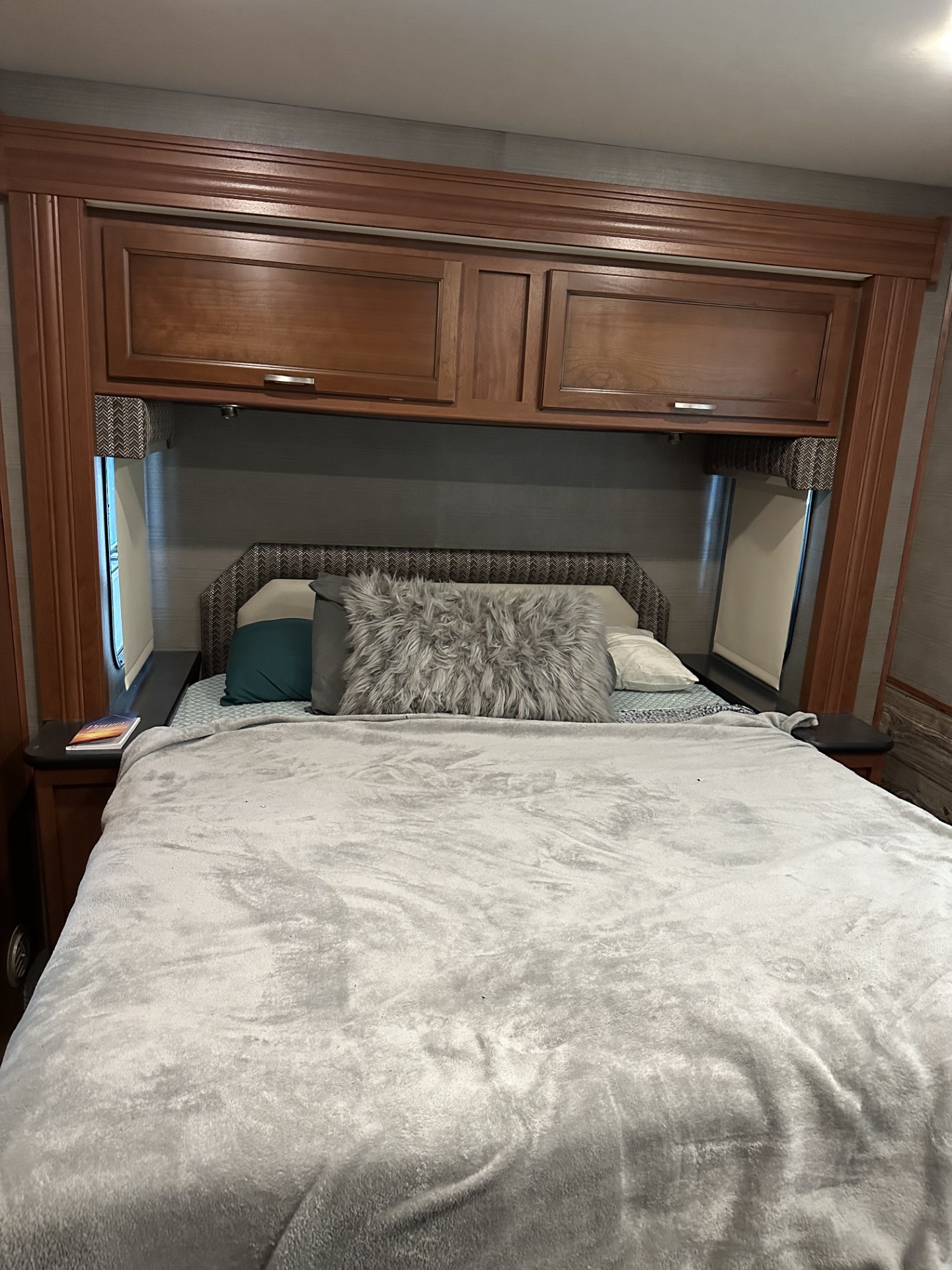 A comfortable RV rental bedroom with a grey blanketed bed, decorative pillows, and practical built-in wood overhead storage cabinets.. Holiday Rambler Admiral XE 2016