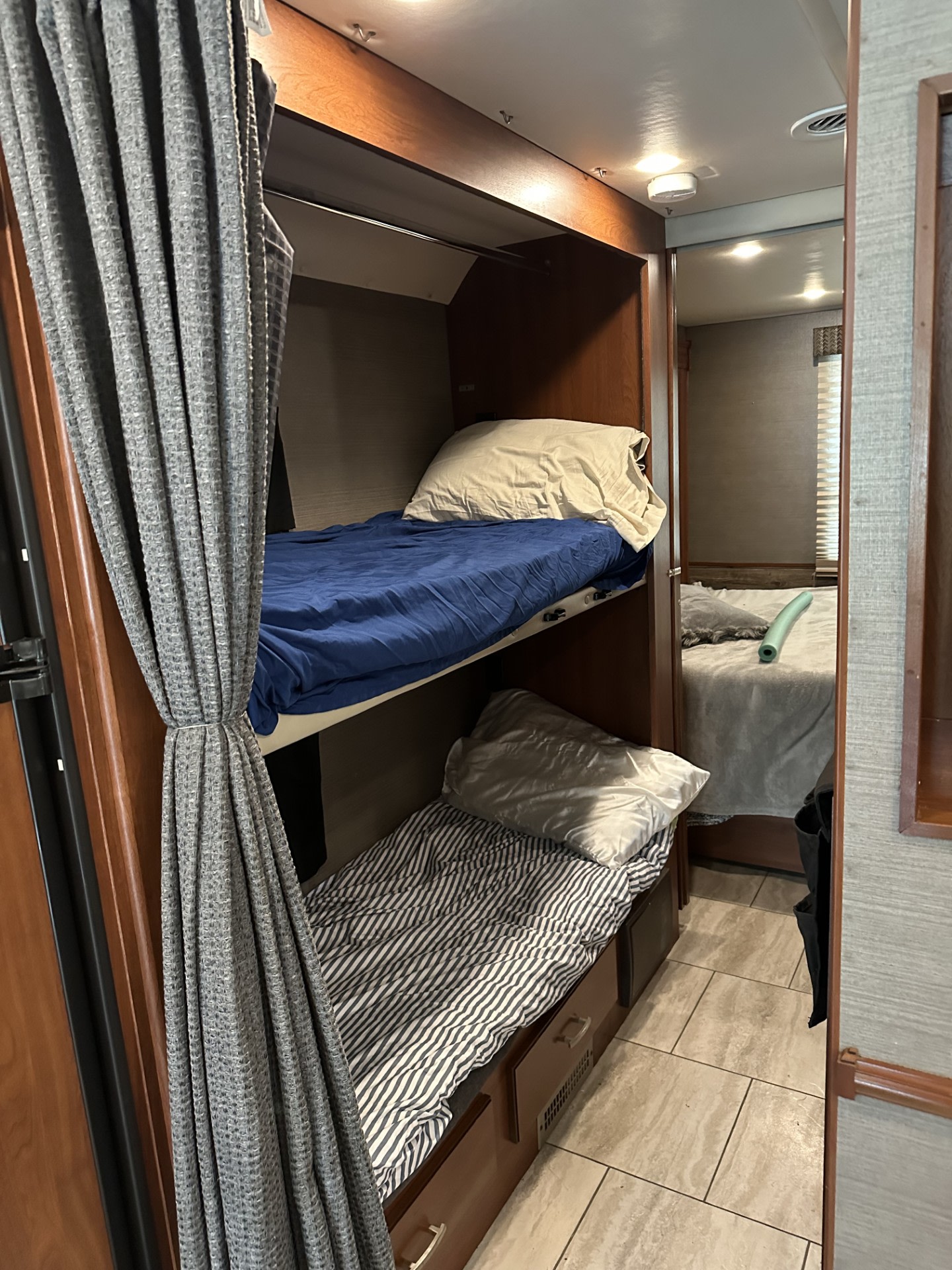 An RV rental's interior featuring two comfortable bunk beds with curtains and a glimpse of an additional sleeping area.. Holiday Rambler Admiral XE 2016