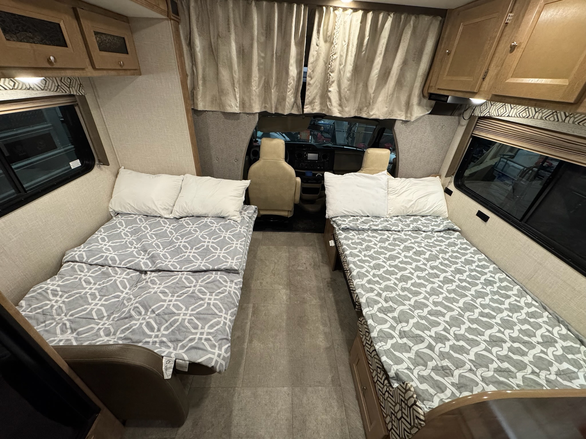 RV rental interior featuring two cozy twin beds with patterned quilts, overhead cabinets, and a clear view of the front cabin.. Coachmen Leprechaun 2020