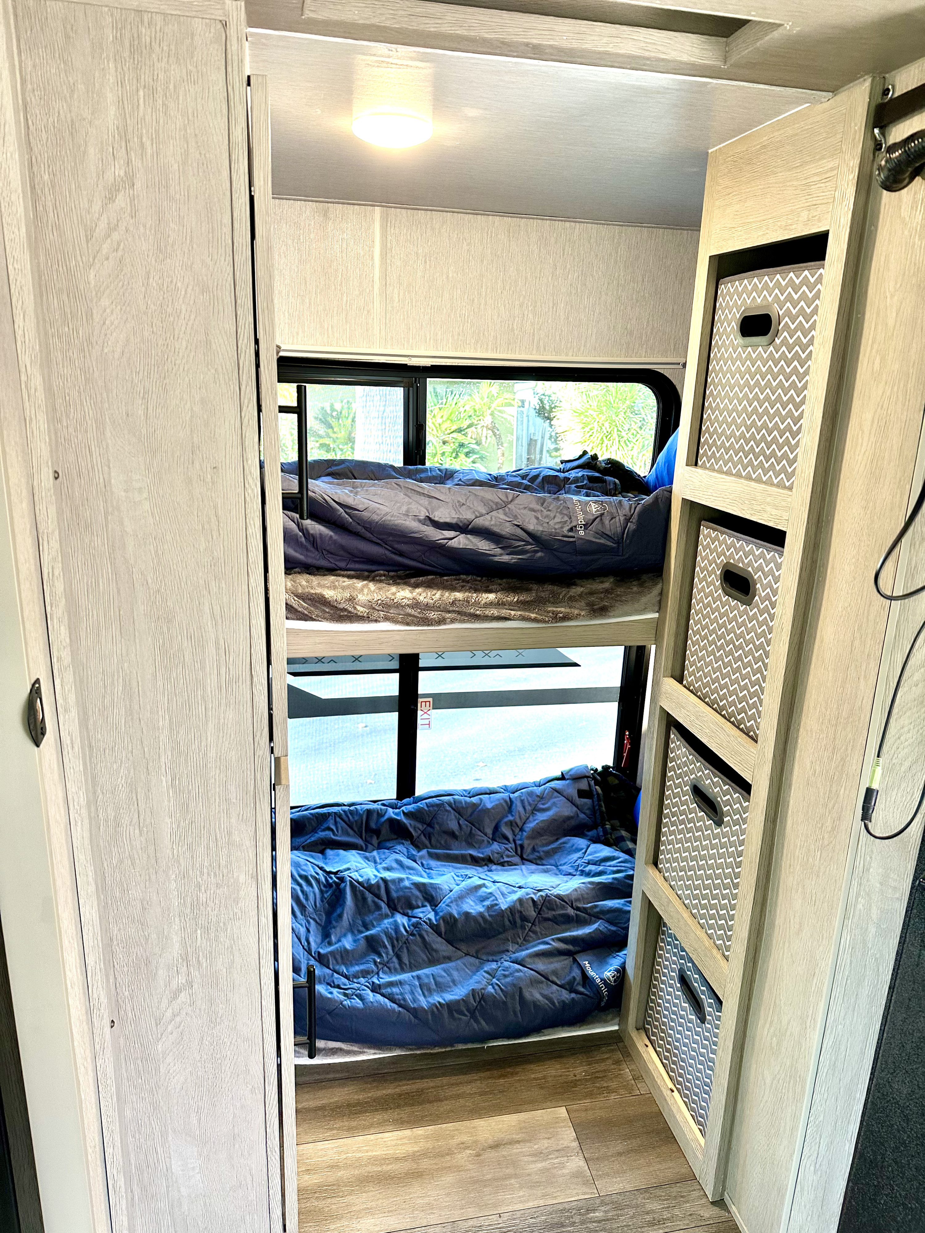 Cozy RV rental bunk beds with windows, sleeping bags, and built-in storage bins. Perfect for family travel accommodation.. Forest River T2510HBL 2024