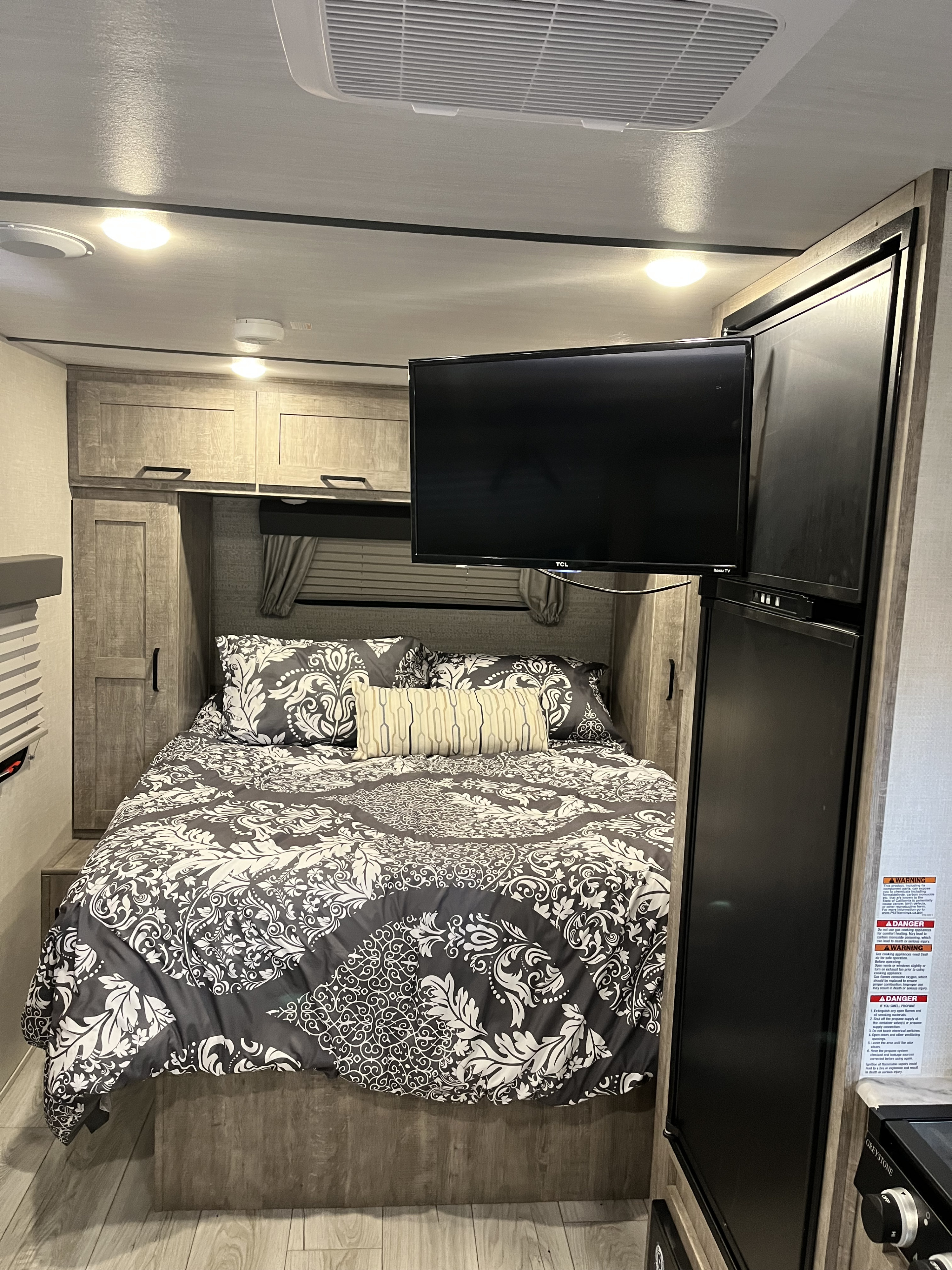Cozy RV rental interior featuring a comfortable bed with patterned bedding, a wall-mounted TV, and a built-in refrigerator.. Forest River Surveyor Legend 2023