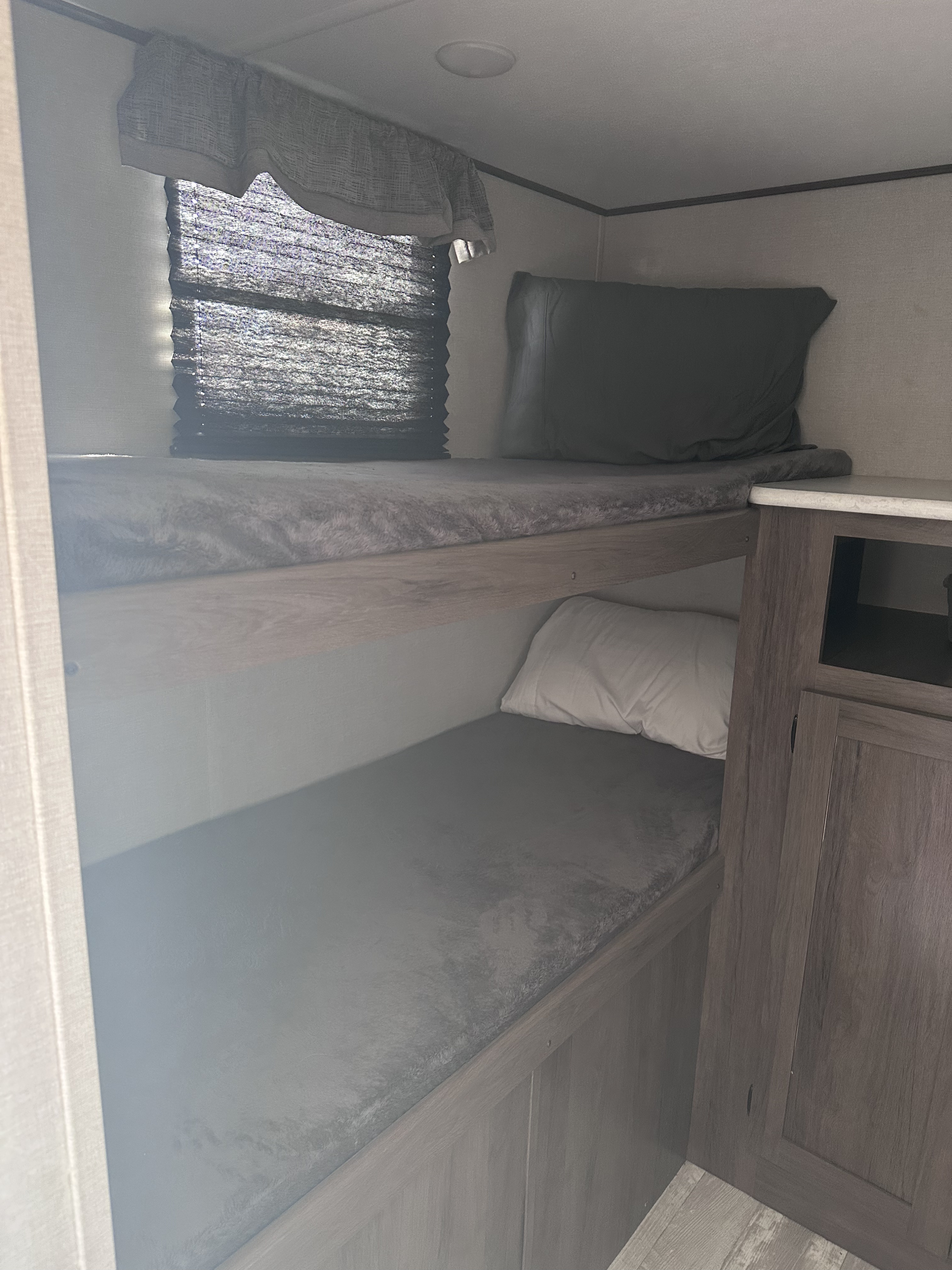 RV rental: Bunk beds with grey mattresses, a window with pleated blinds, and wood cabinetry for a cozy interior.. Forest River Avenger 29QBS 2021