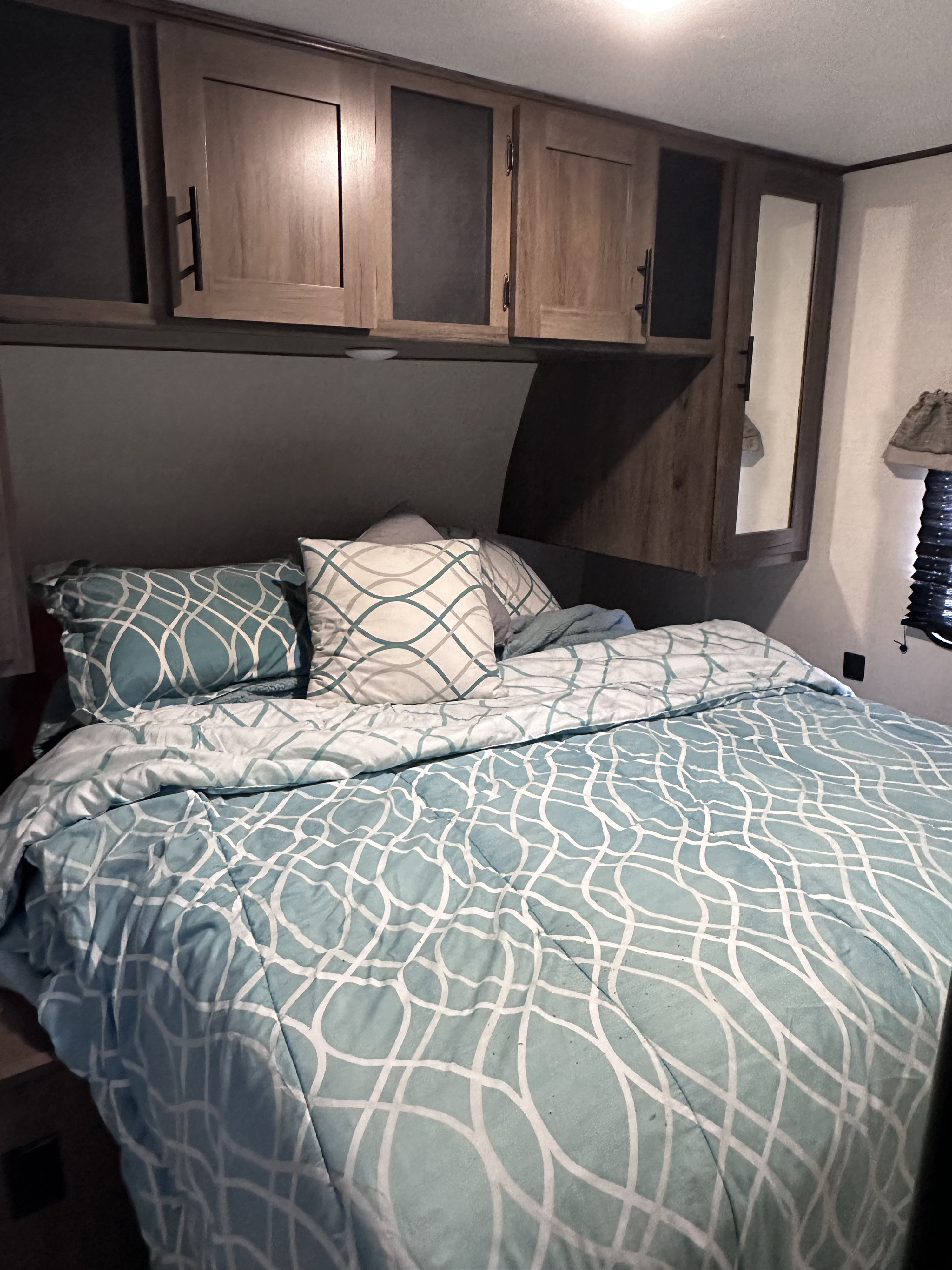 Comfy RV rental bedroom featuring patterned blue bedding, pillows, overhead storage cabinets, and a mirrored closet.. Forest River Avenger 29QBS 2021