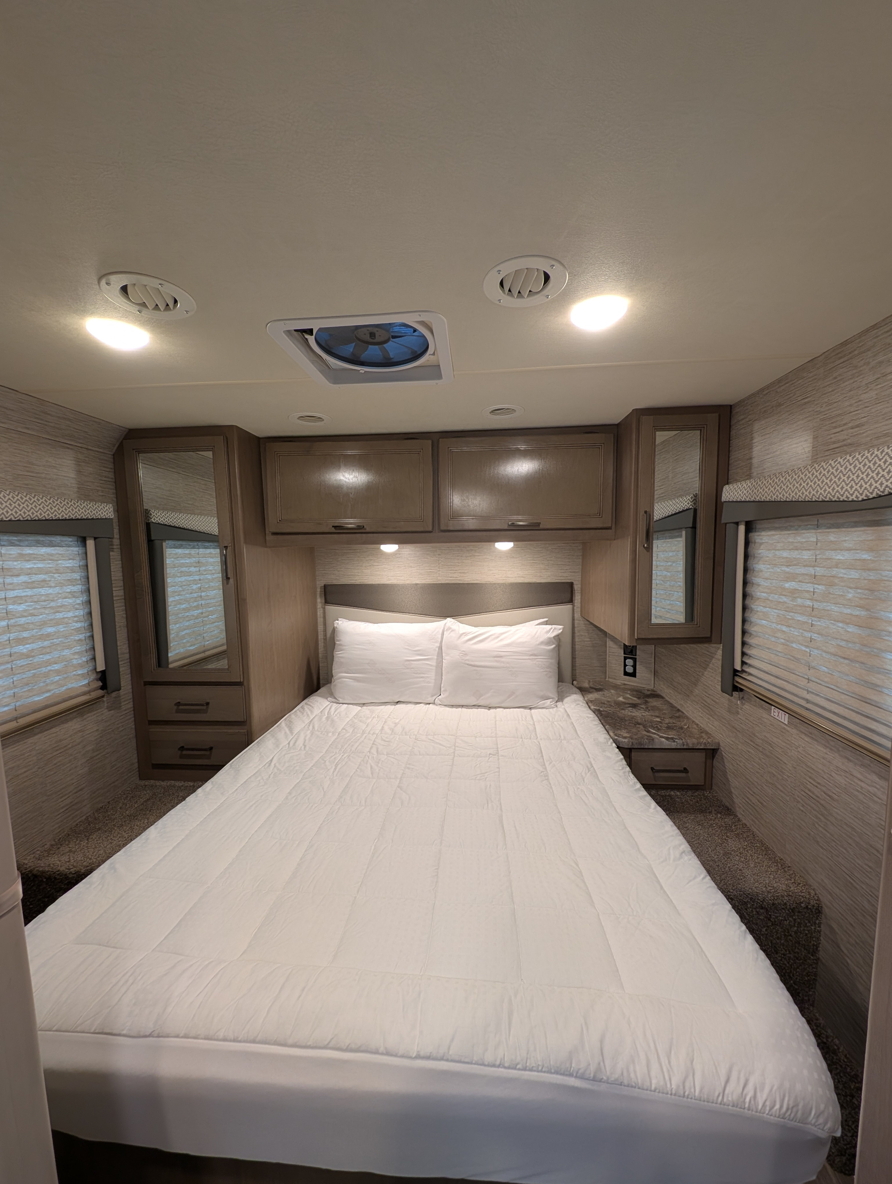 RV rental bedroom: cozy space with white bedding, overhead storage, mirrored cabinets, and window blinds.. Thor Four Winds 2021