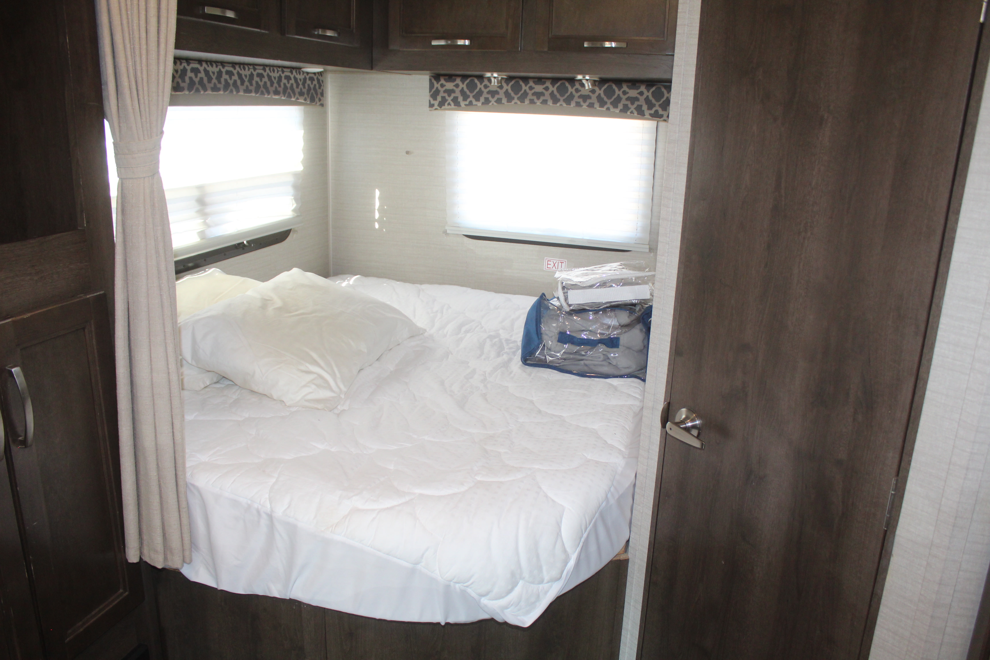 Cozy RV rental bedroom with white bed, overhead cabinets, windows, and safety exit sign, ready for adventure.. Jayco Redhawk 2019