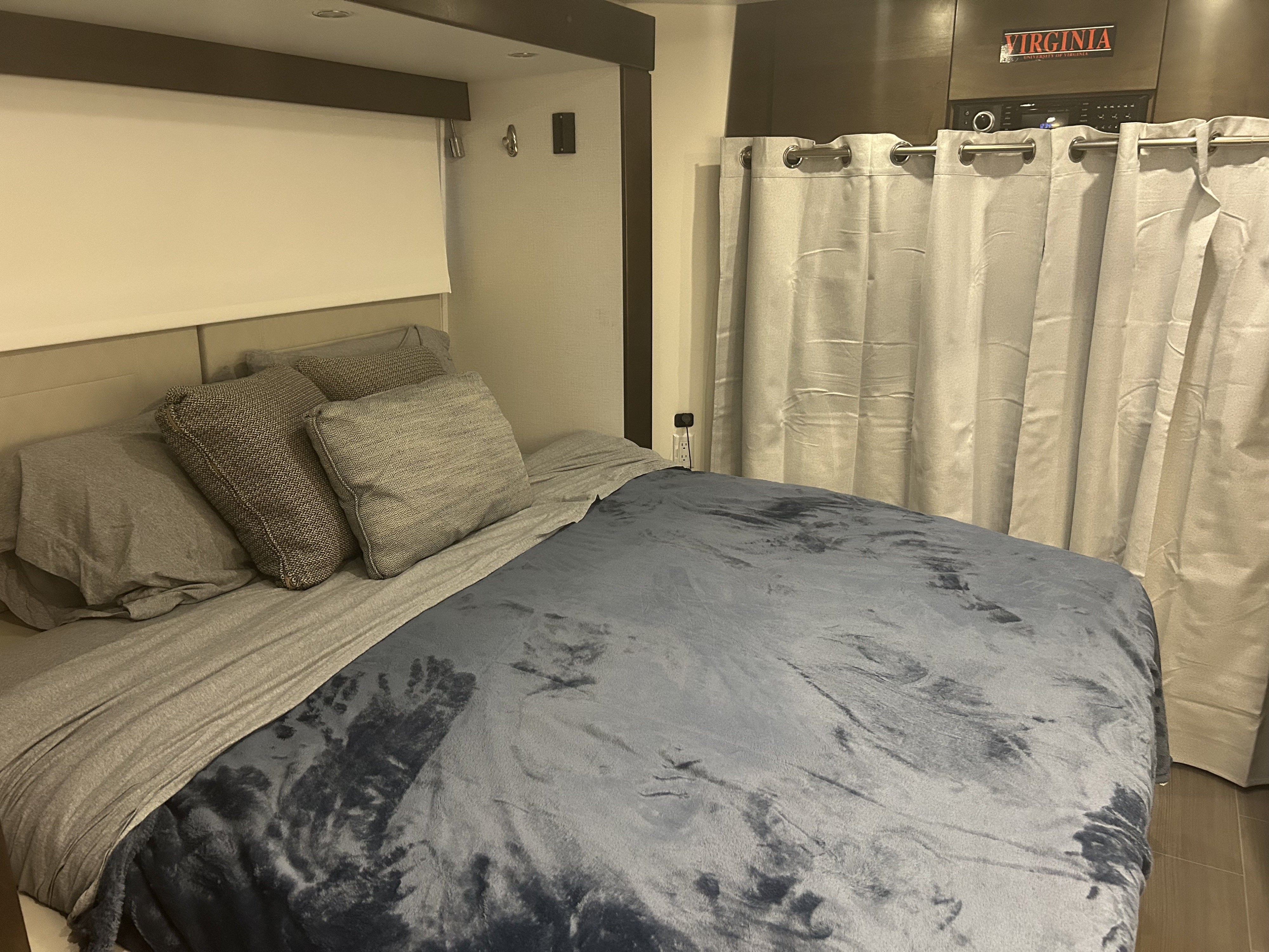 Cozy RV rental bedroom featuring a comfortable bed with a blue blanket, grey linens, and privacy curtains.. Leisure Travel Unity Fx 2019
