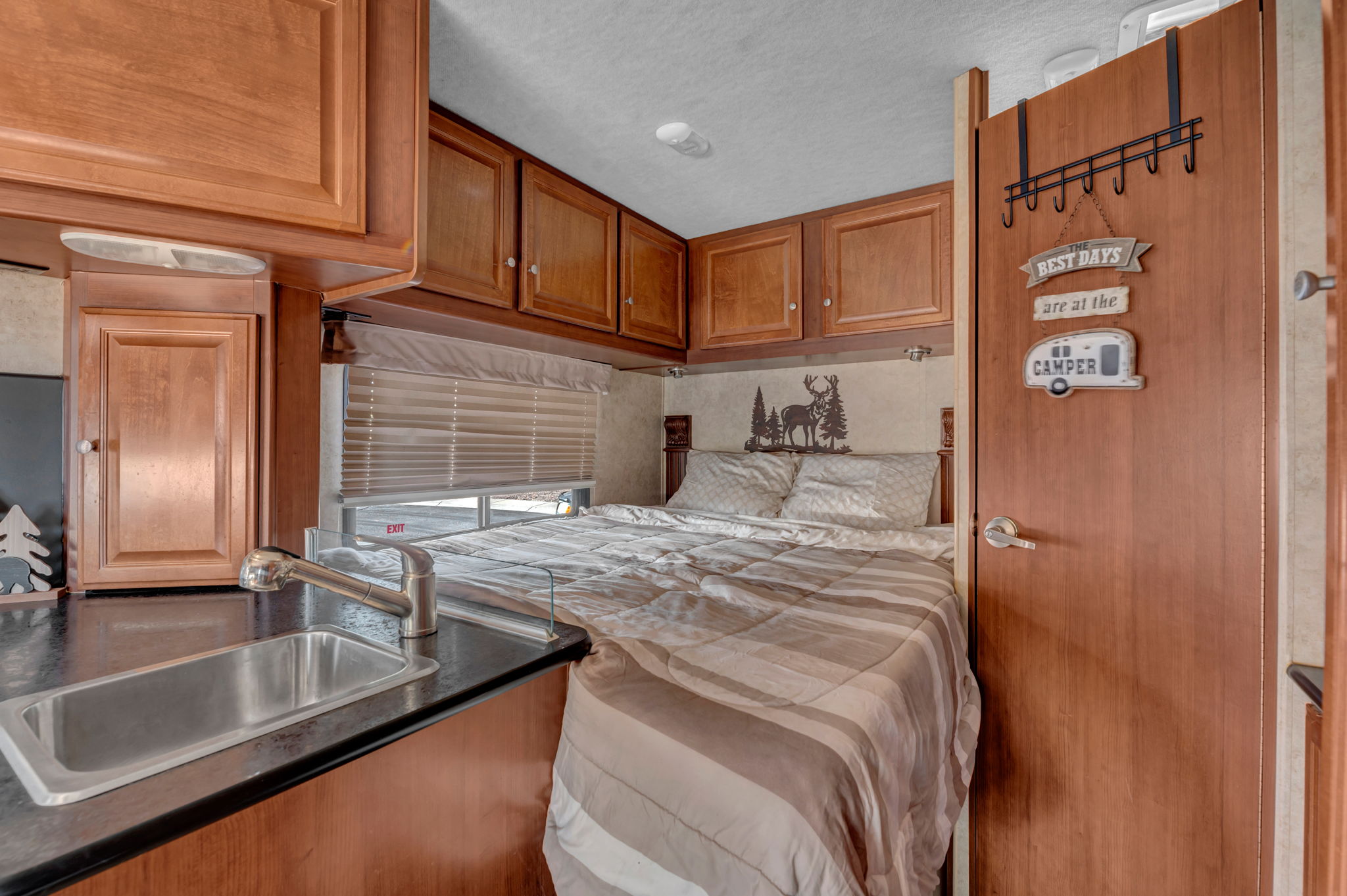 Interior view of a cozy RV rental, showing the bed and compact kitchen area with sink.. Jamboree Searcher 2014