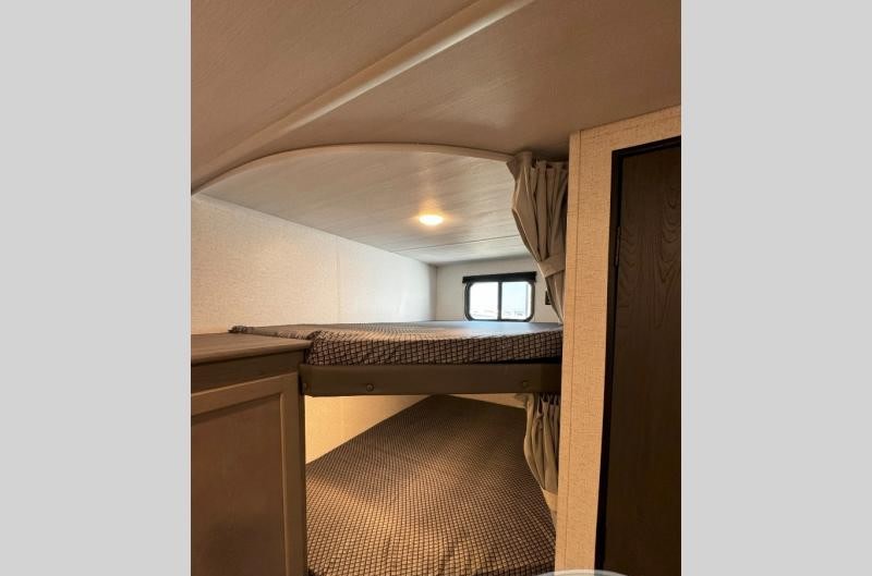 This RV rental offers a cozy interior with two comfortable bunk beds and a window, ideal for family sleeping arrangements.. Keystone Hideout 2025