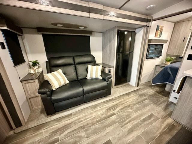 Modern RV rental interior: spacious living area with sofa, refrigerator, and private bedroom for comfortable travel.. Keystone Passport 2021