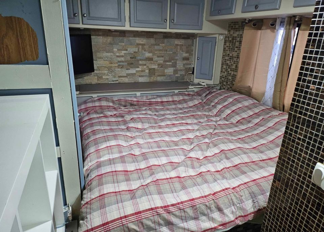 Inside an RV rental: a cozy bedroom with red and gray plaid bedding, overhead cabinets, and a mosaic tiled wall.. Gulf Stream Crescendo 2005