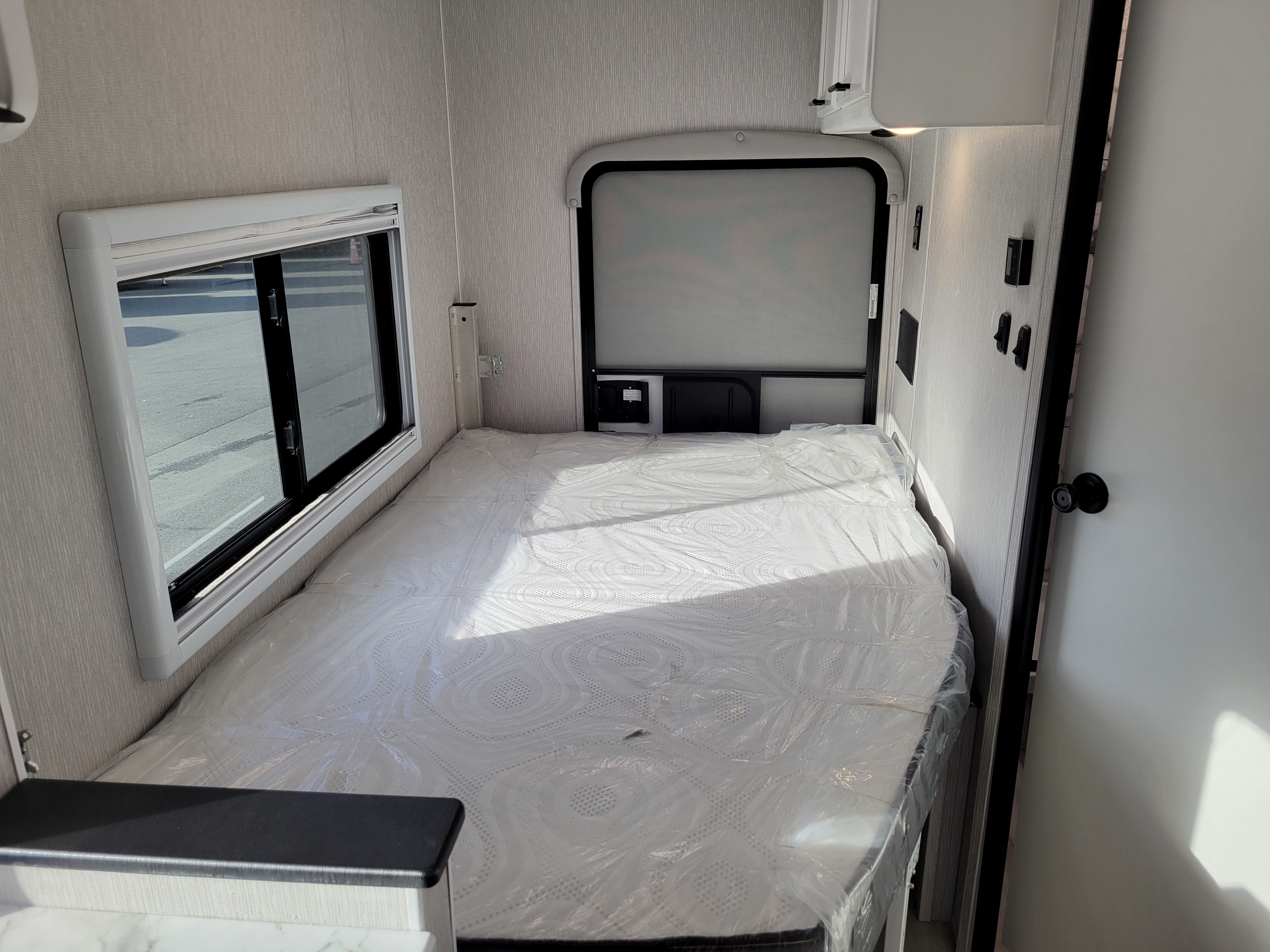 Inside an RV rental: a clean, compact bedroom with a fresh, plastic-wrapped mattress and window view for your travels.. Forest River Cross Trail 21XG 2023