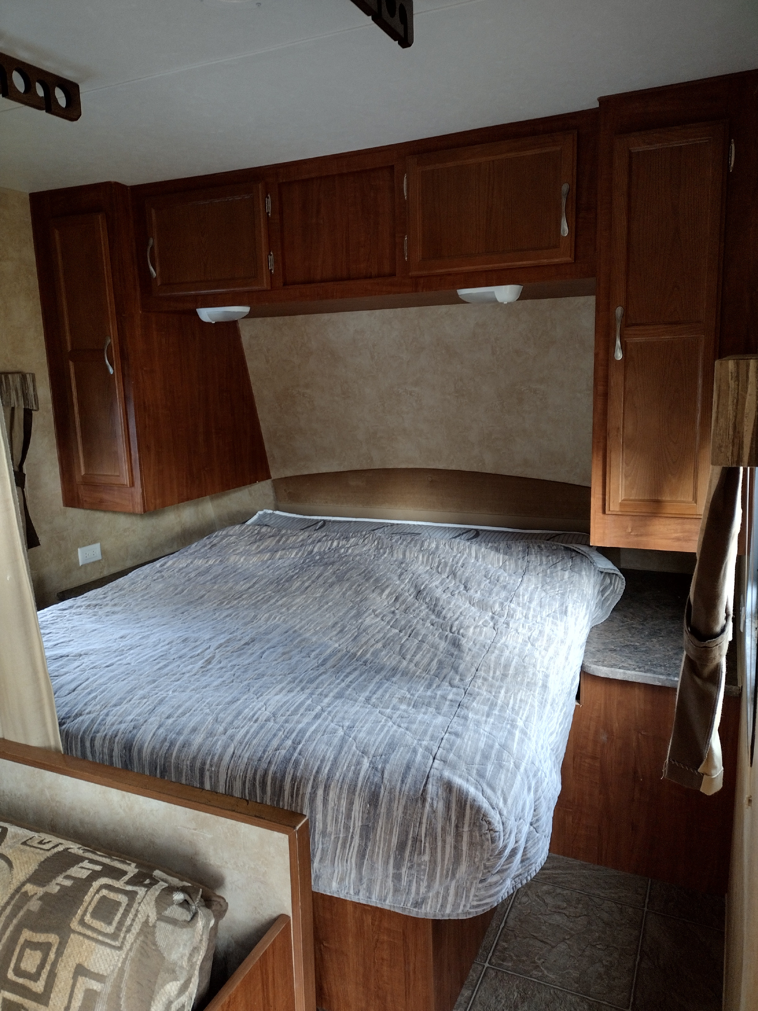 Comfortable RV rental bedroom featuring a large bed, overhead wood cabinets, and built-in lights for cozy travel.. Jayco Jay Flight Swift 2011