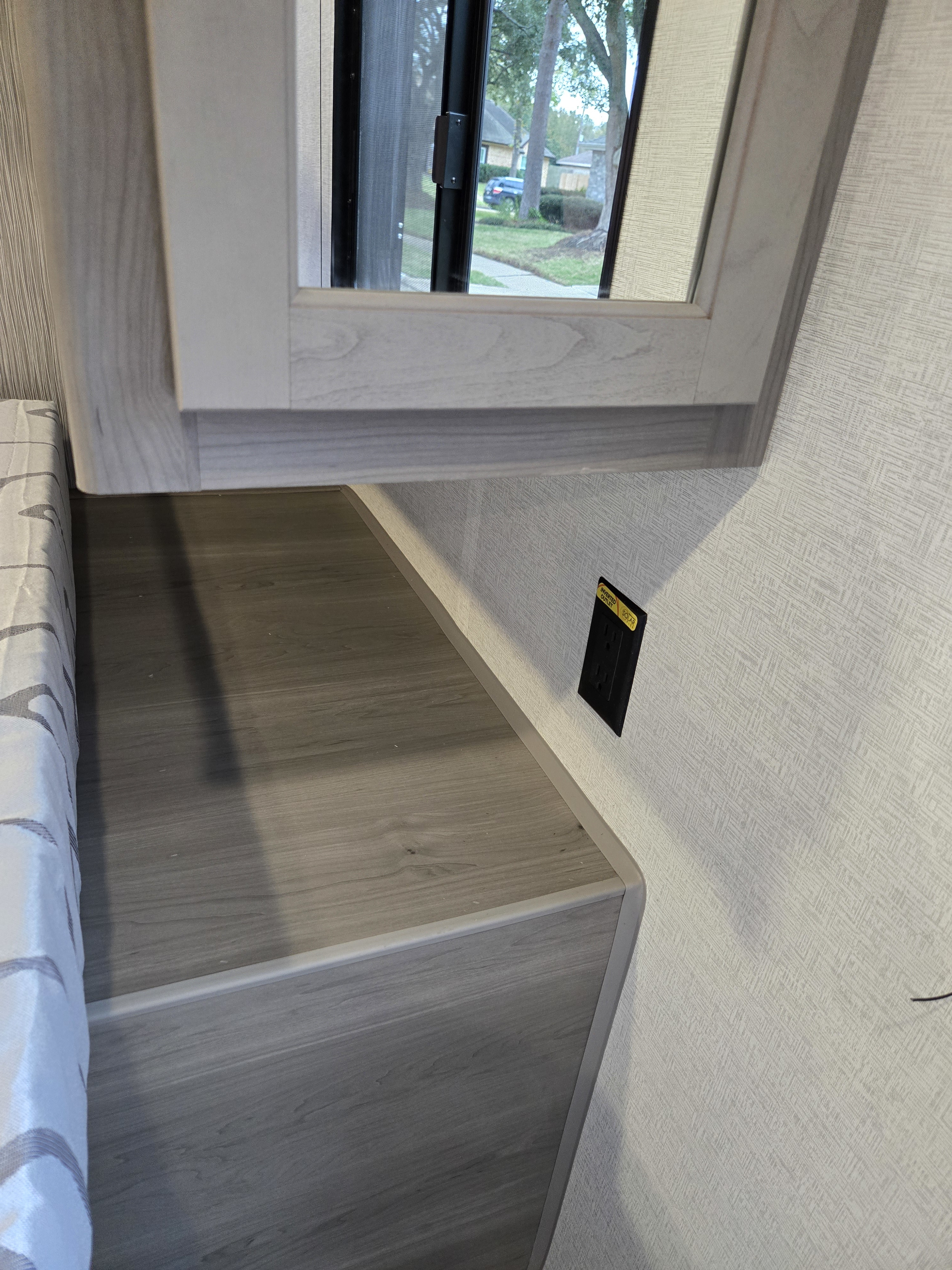 Inside an RV rental, showing a window with an outdoor view, a bed, a side counter, and a solar-powered electrical outlet.. Keystone Hideout 240BH 2025