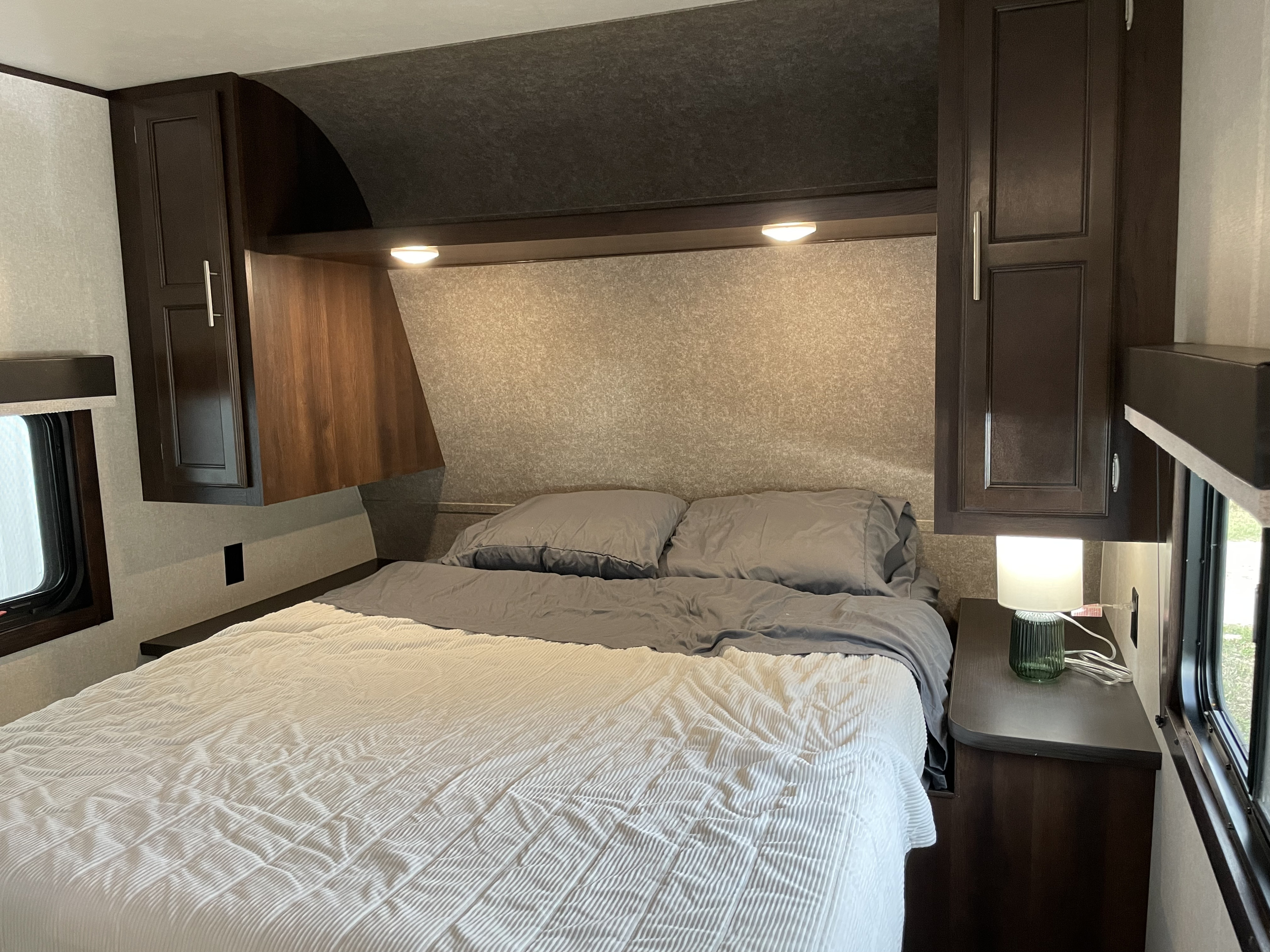 Cozy RV rental bedroom with dark wood cabinets, a comfy bed, and reading lights, perfect for travel.. Jayco Jay Flight 2019