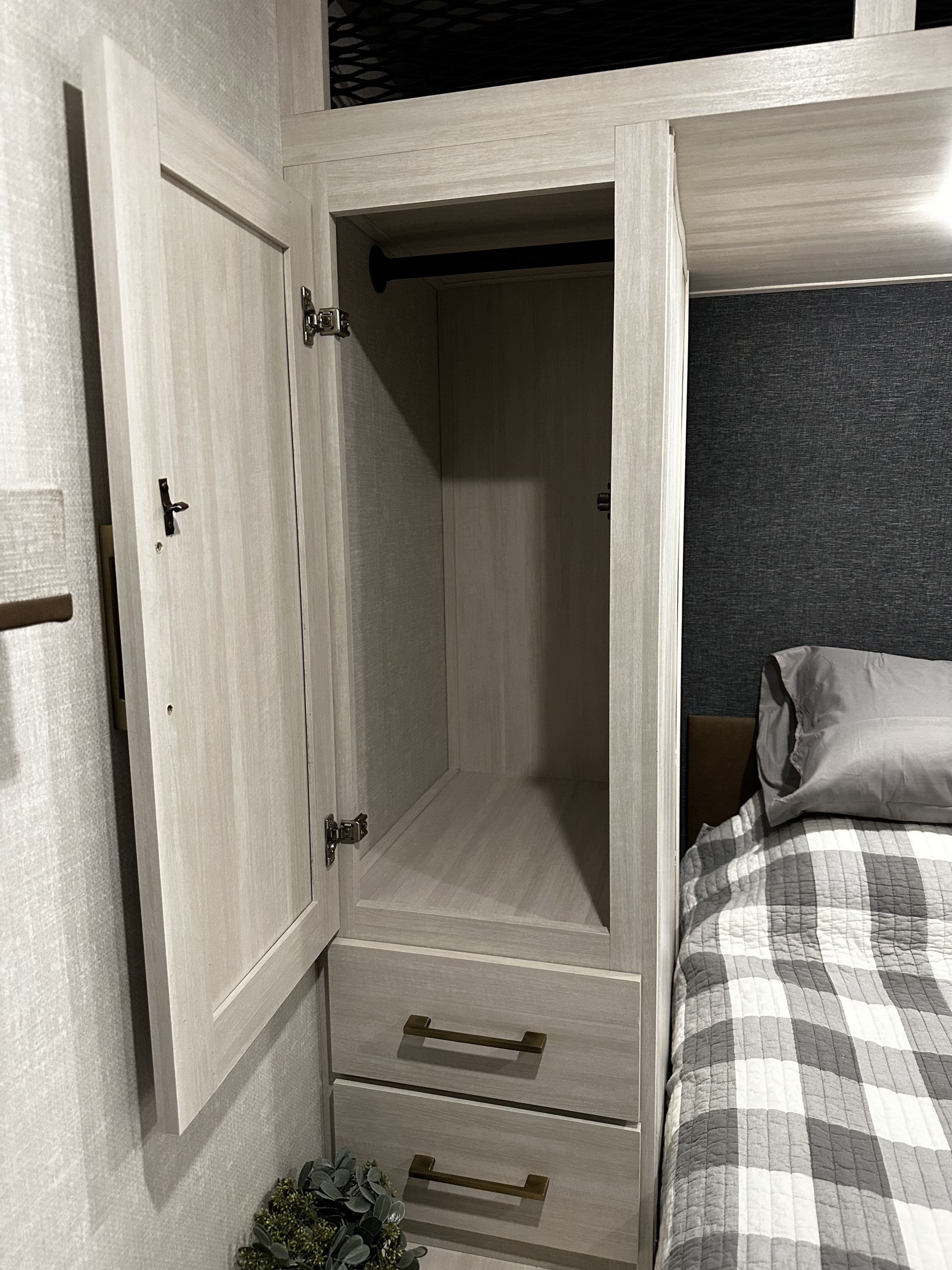 Inside your RV rental, a well-organized bedroom featuring an open wardrobe with a hanging rod, drawers, and cozy bedding.. Forest River Surveyor Legend X 2025