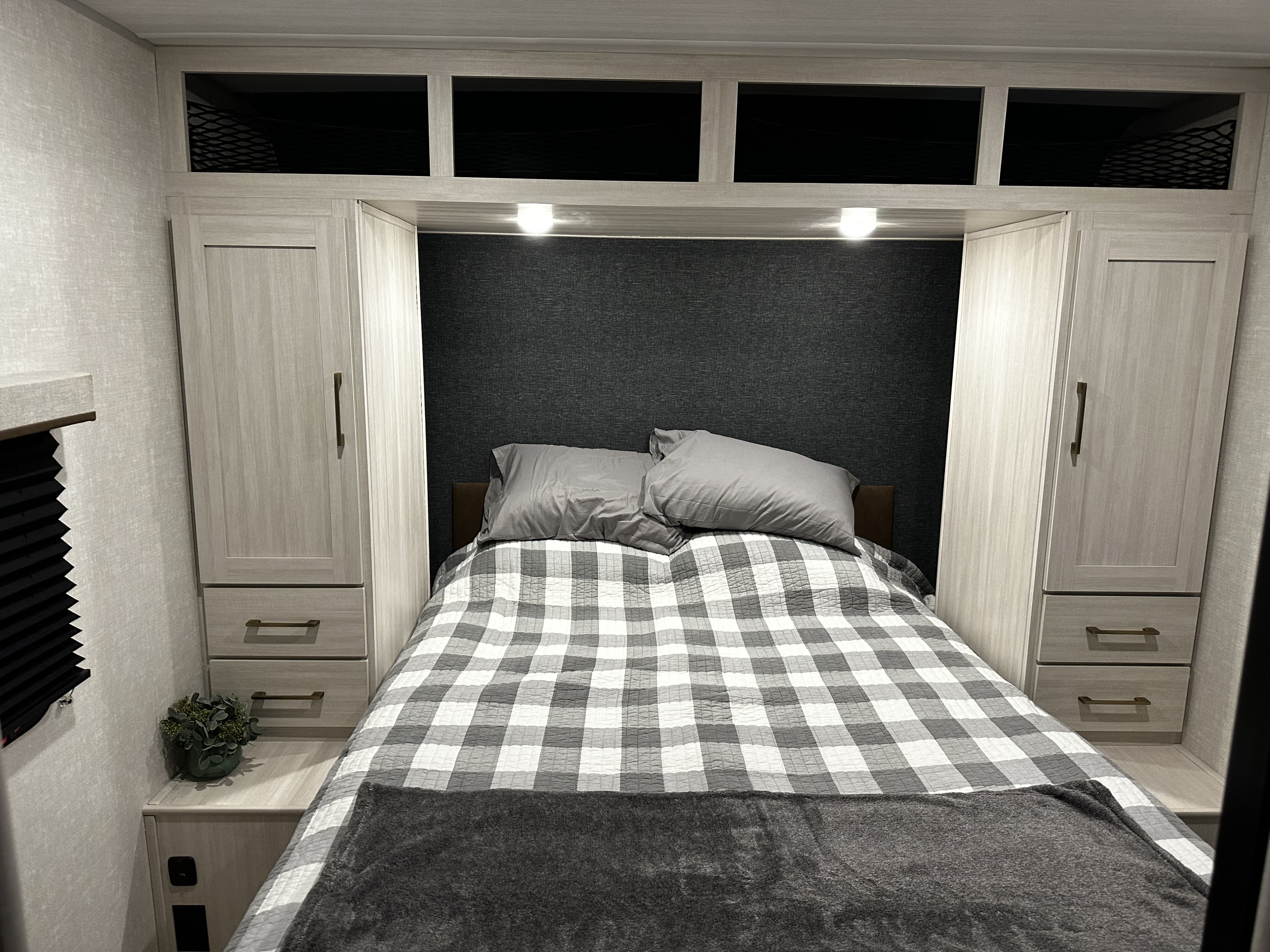 Compact RV rental bedroom with light wood cabinetry, dark gray walls, and a cozy plaid bed, ideal for travel comfort.. Forest River Surveyor Legend X 2025
