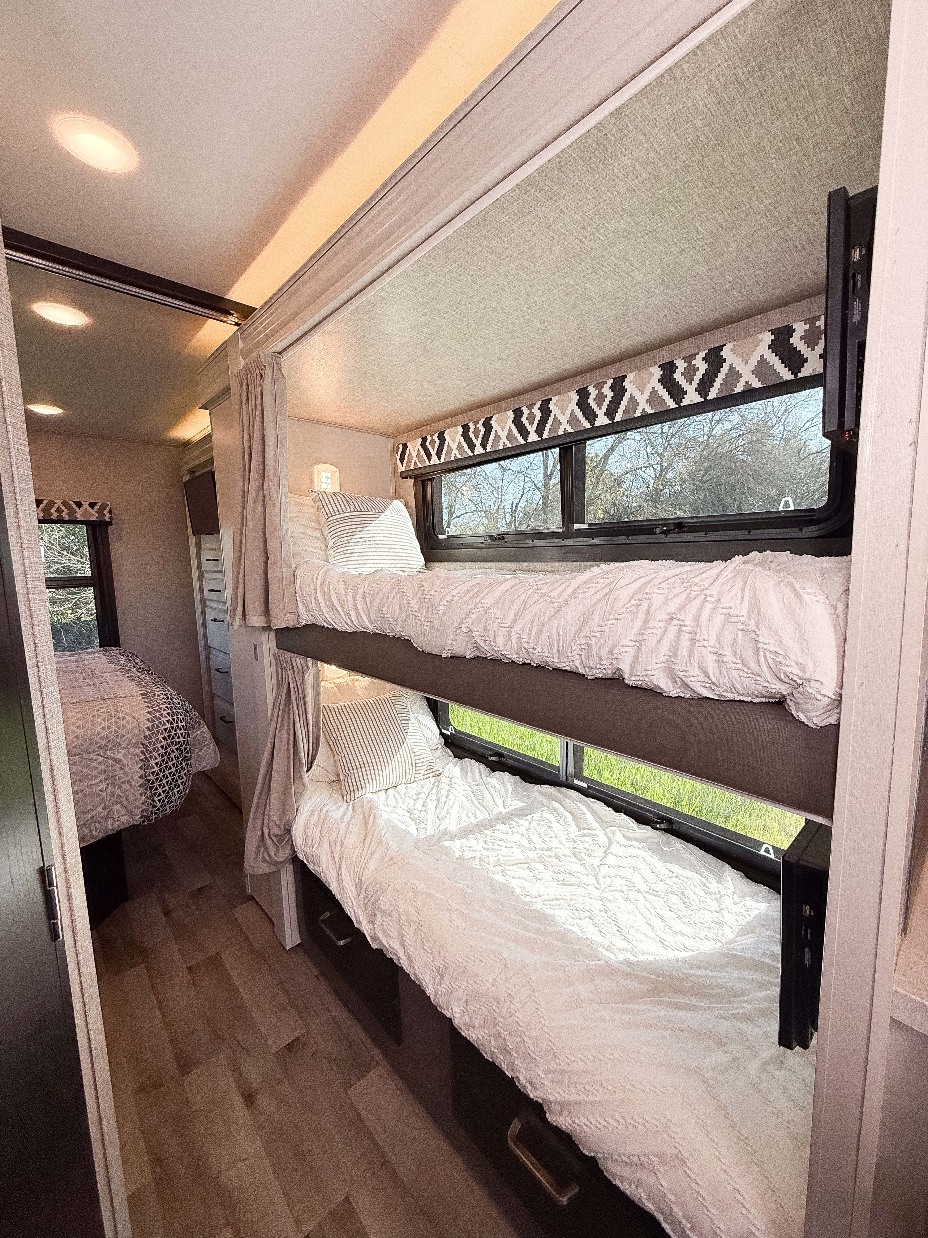 RV rental interior: cozy bunk beds with light bedding, master bed visible, and wood-look floors. Ready for adventures.. Entegra Coach Odyssey 2022