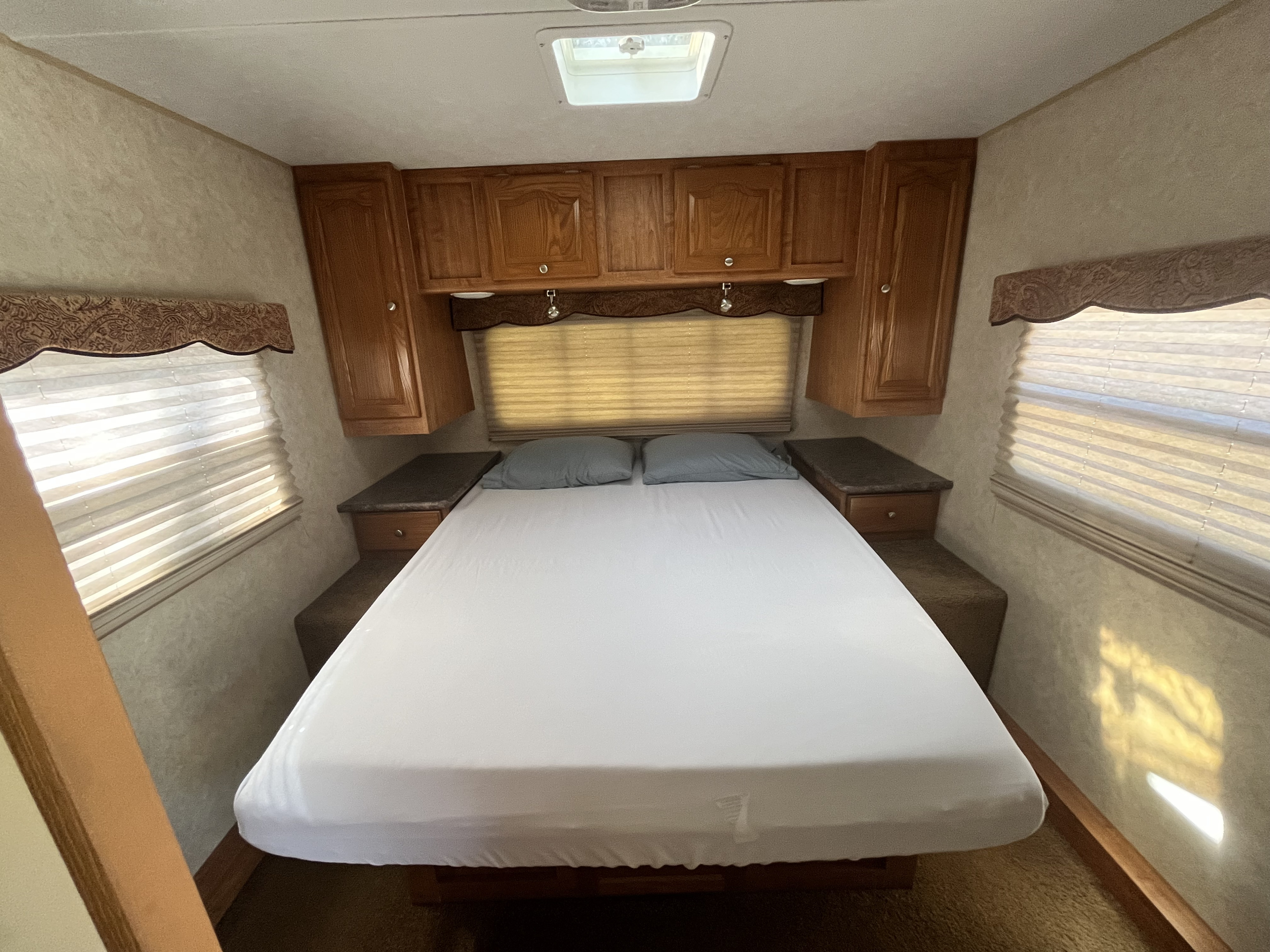 Comfortable RV rental bedroom featuring a large bed, overhead storage, and natural light, ideal for travel adventures.. Forest River Rockwood Signature Ultra 2010