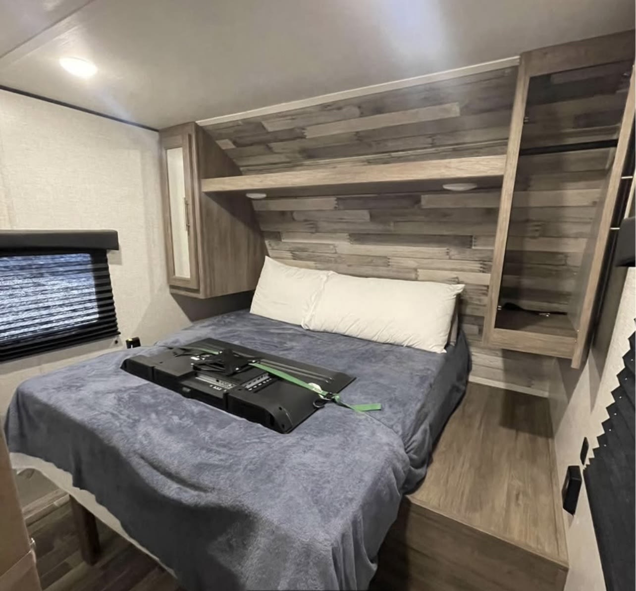 This cozy RV rental bedroom offers a bed, TV mount, window, and wood-paneled storage. Ideal for travelers.. Crossroads RV Zinger 2021