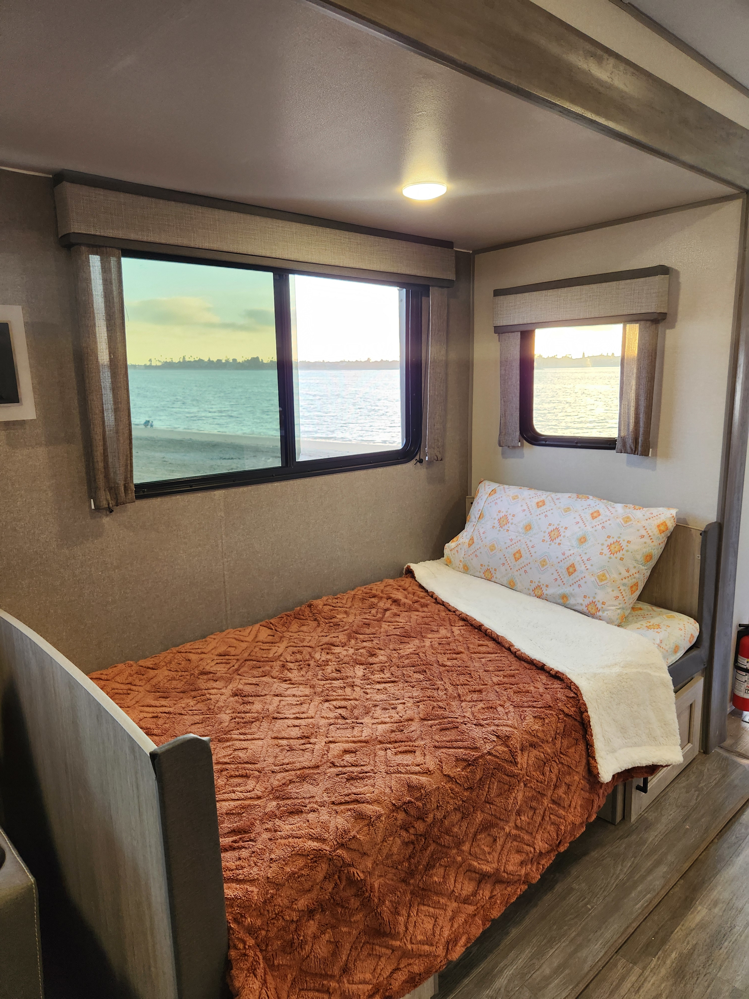 Serene RV rental bedroom features a comfy bed, waterfront views from large windows, and natural light.. Forest River Aurora Aurora 2024