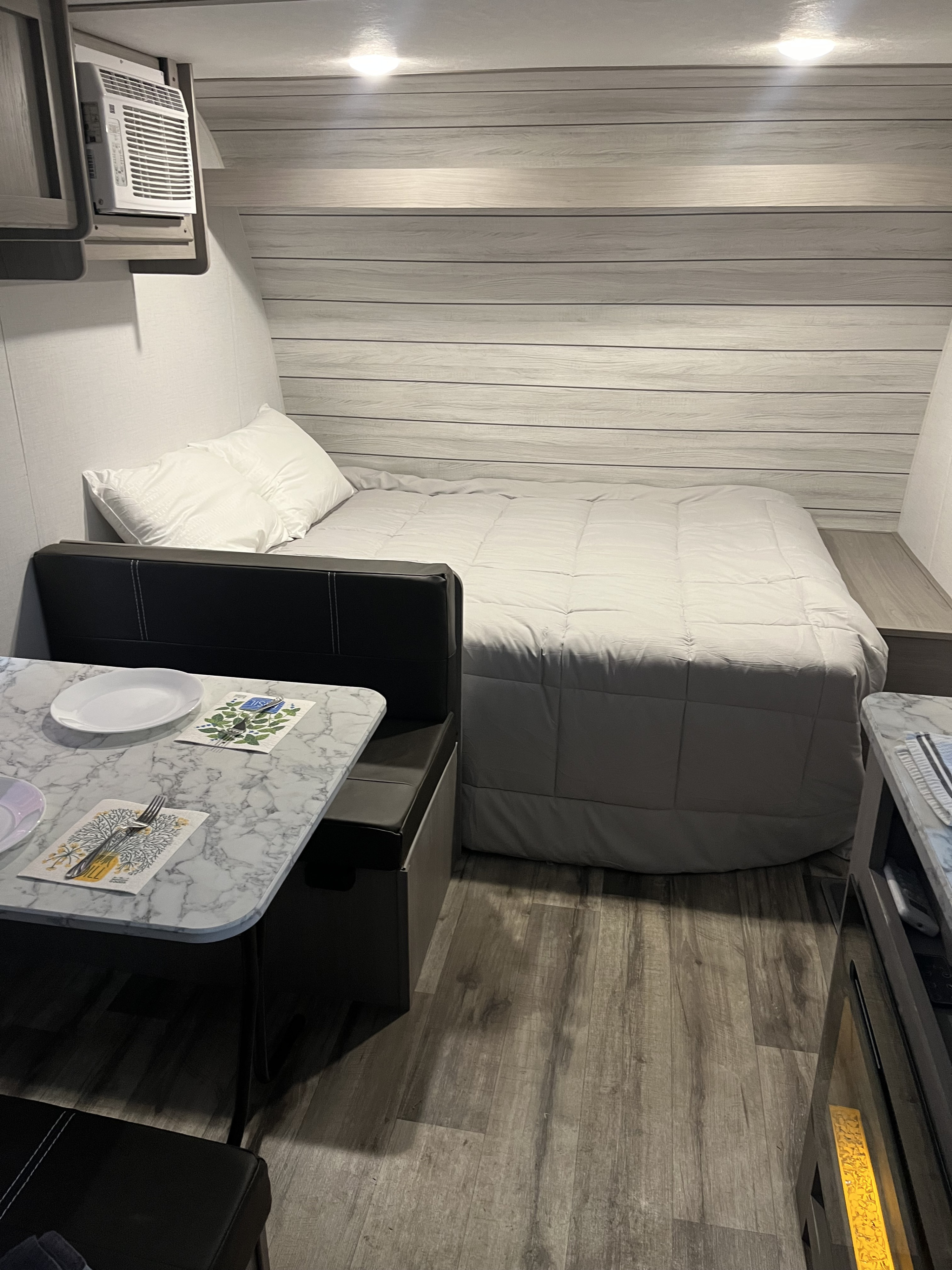 This rv rental features a cozy interior with a light gray bed, a marble-top dining booth, and an overhead AC unit.. Dutchmen Coleman Lantern LT 17B 2024