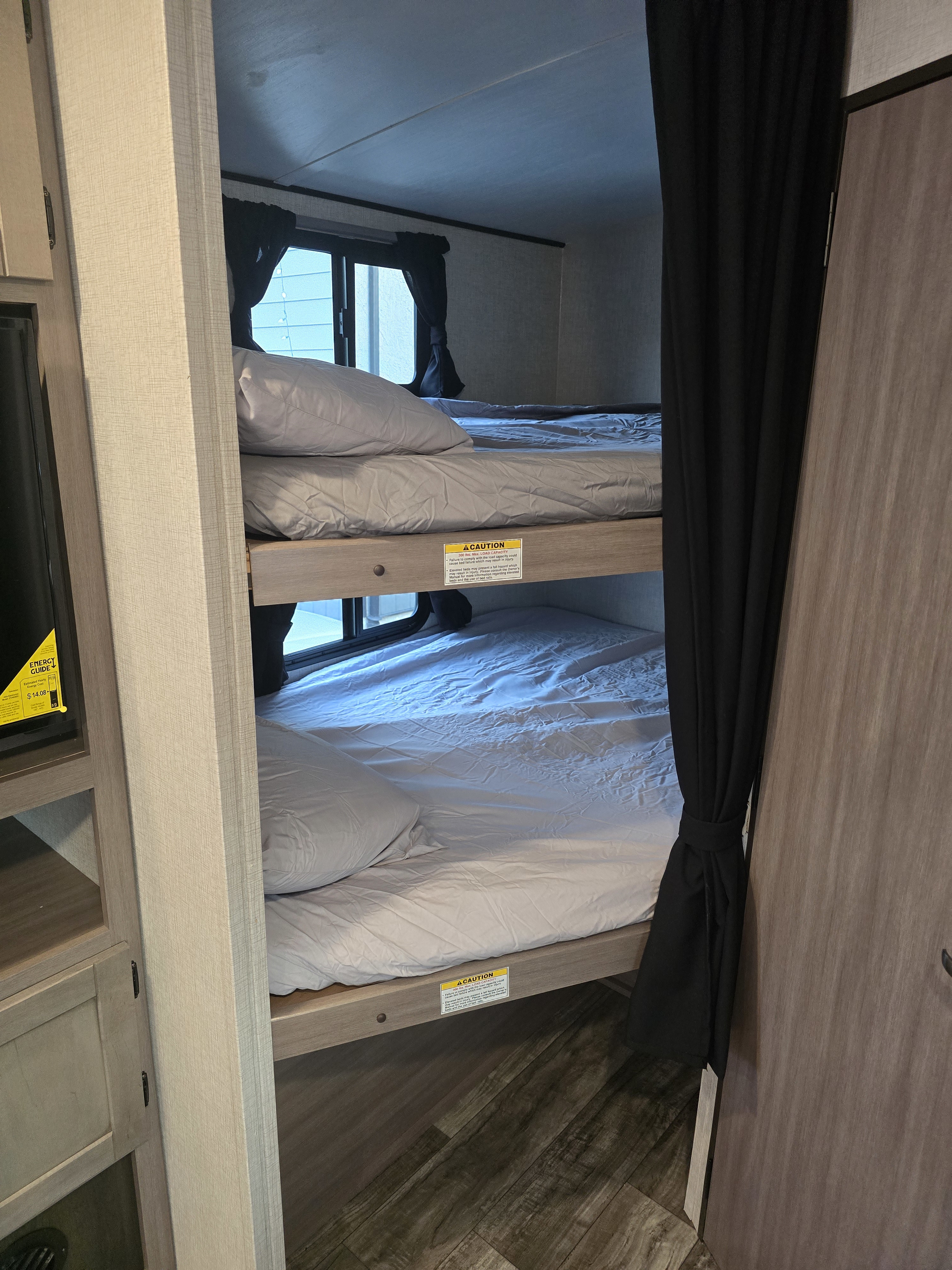 RV rental interior showcasing cozy bunk beds, each with fresh linens. Privacy curtains and safety warning labels are visible.. Crossroads RV Sunset Trail Super Lite 2022