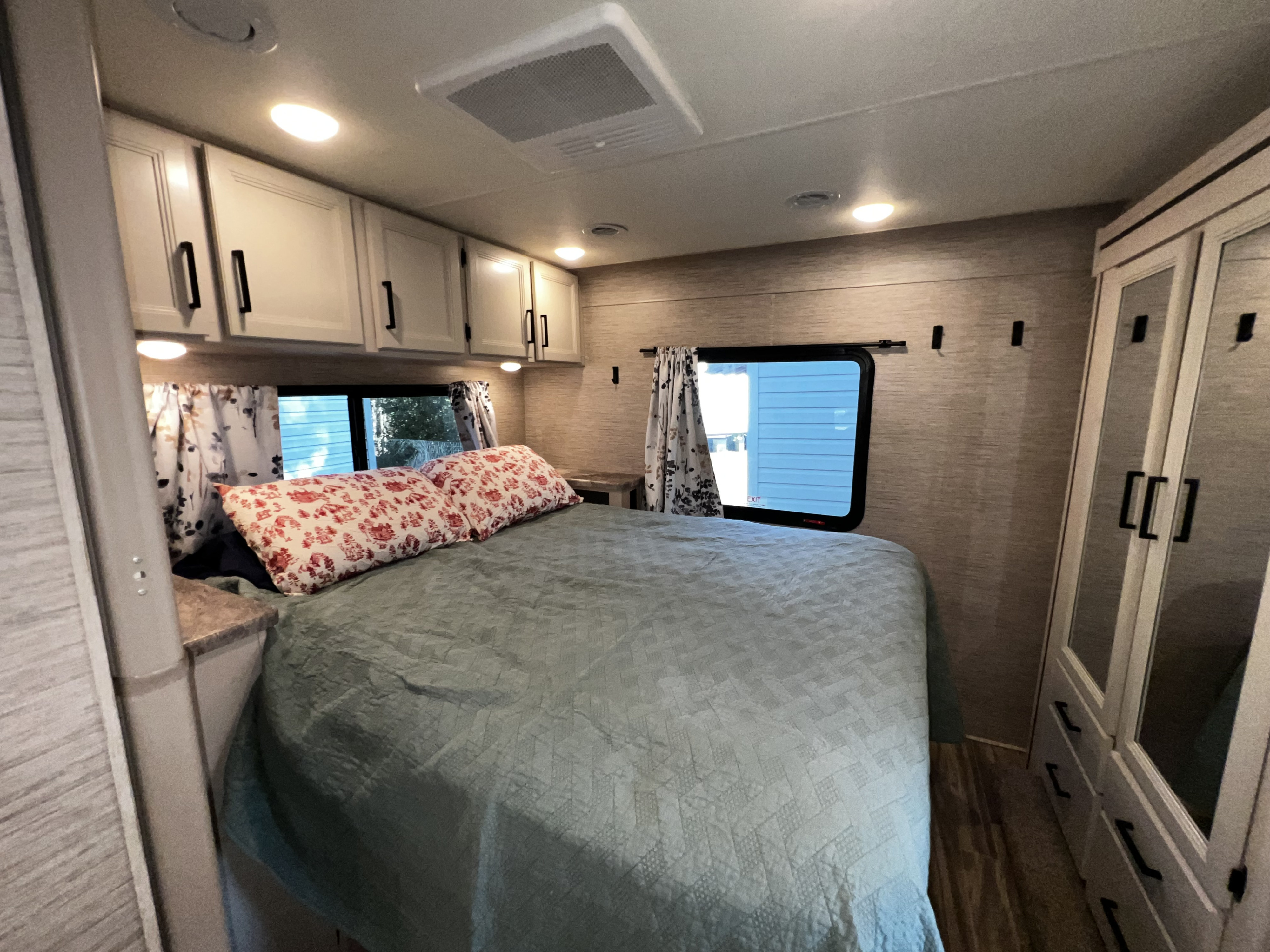 Interior of an RV rental bedroom, featuring a large bed with pillows, cabinets, and a mirrored wardrobe. Ideal for travel.. Thor Four Winds 2022