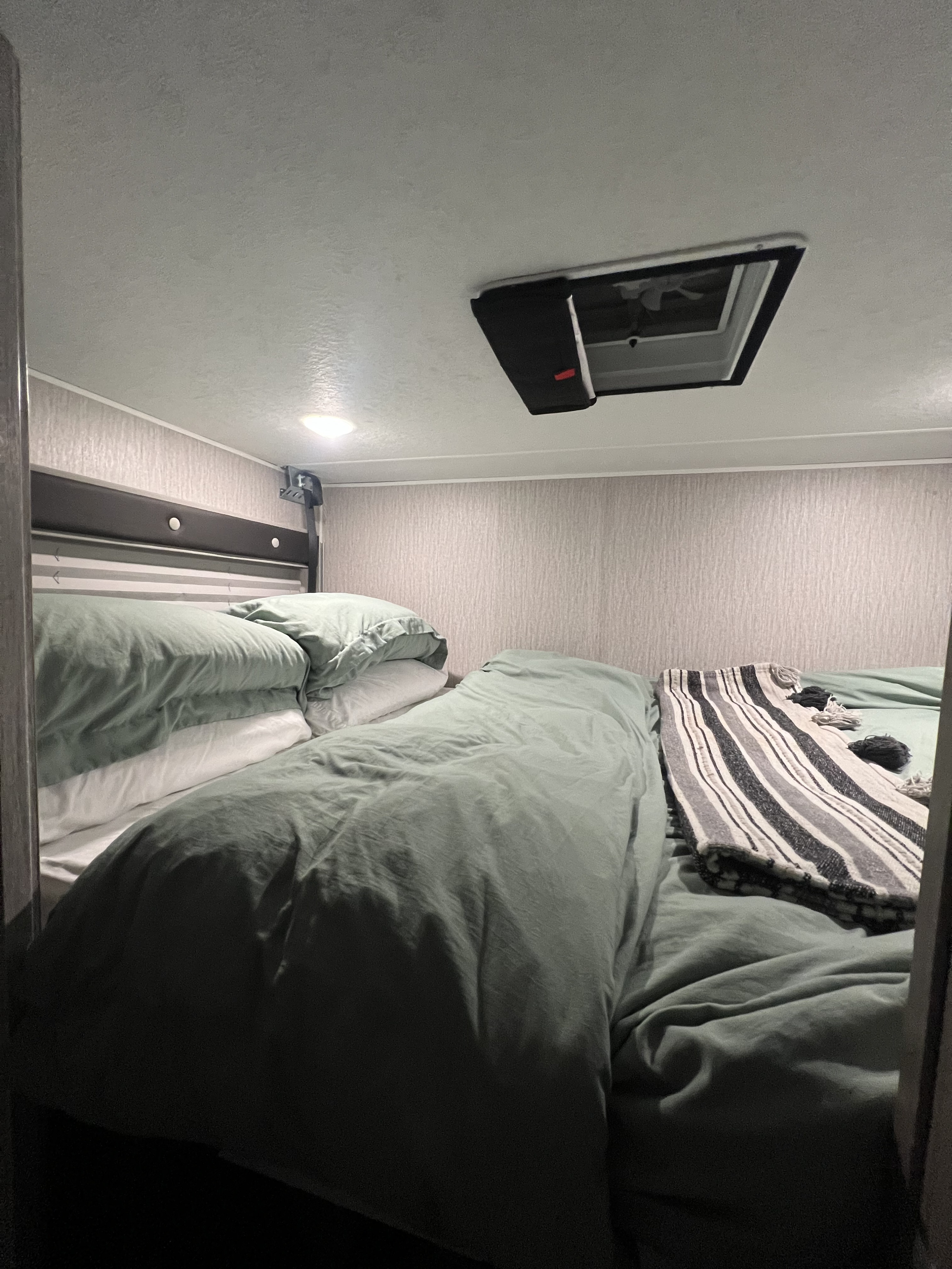 Cozy RV rental bedroom with two bunks, sage green bedding, light fixture, and roof vent.. Coachmen Crosstrail 20XG 2022