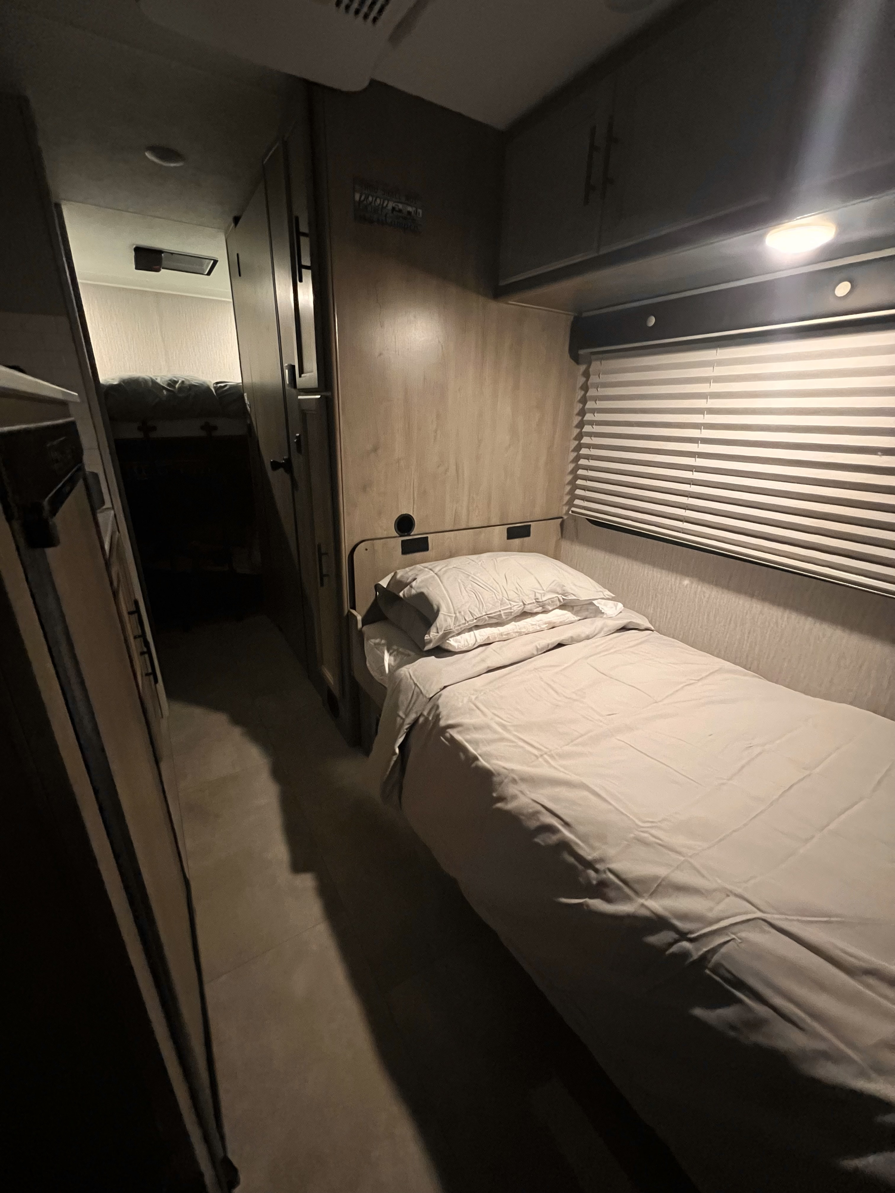 An RV rental features a well-lit single bed, window, and built-in cabinetry, offering a comfortable sleeping space.. Coachmen Crosstrail 20XG 2022