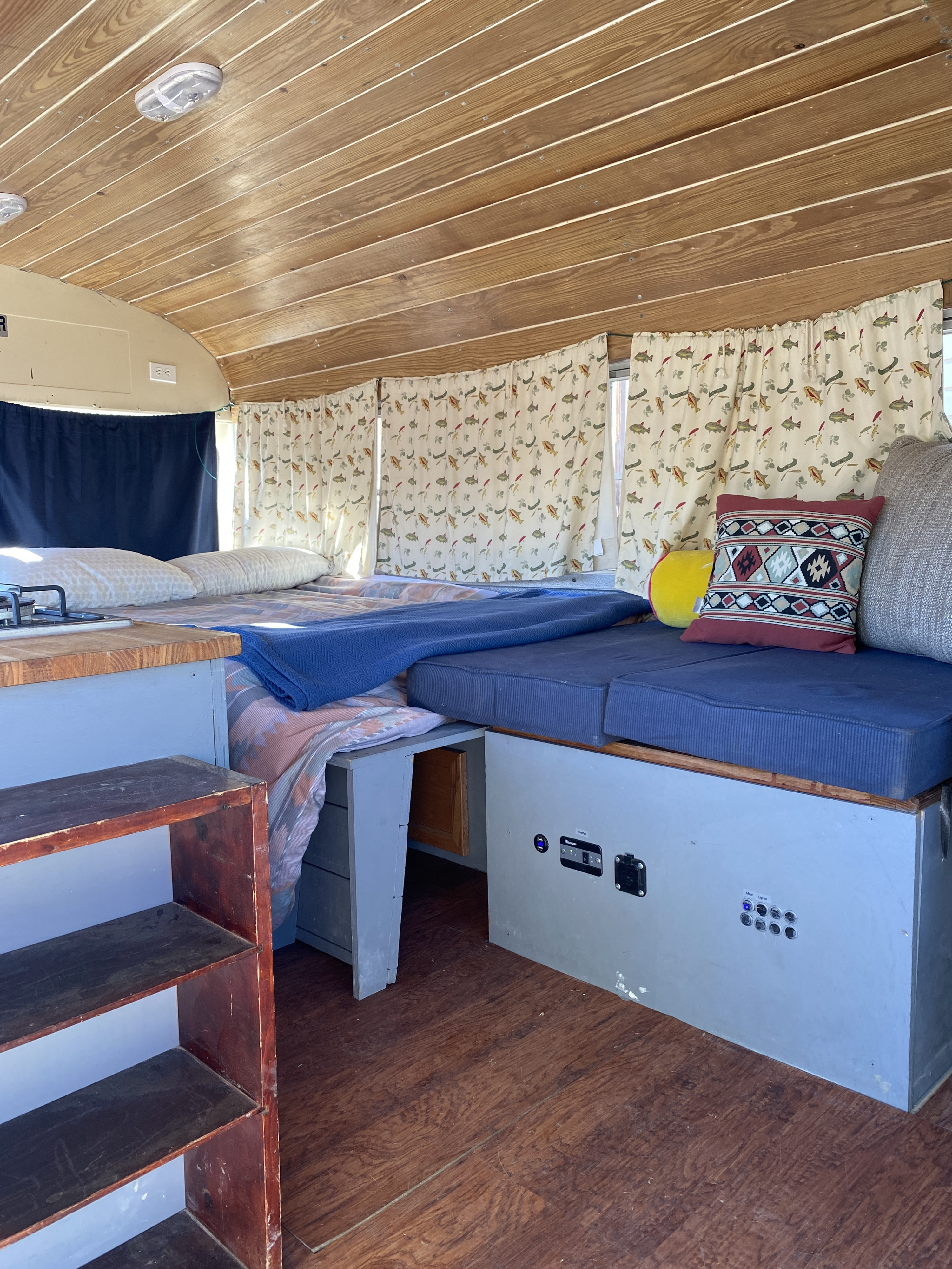Step inside this cozy RV rental with wooden ceilings, a comfy bed, patterned curtains, and a compact living area.. GMC Vandura 1986