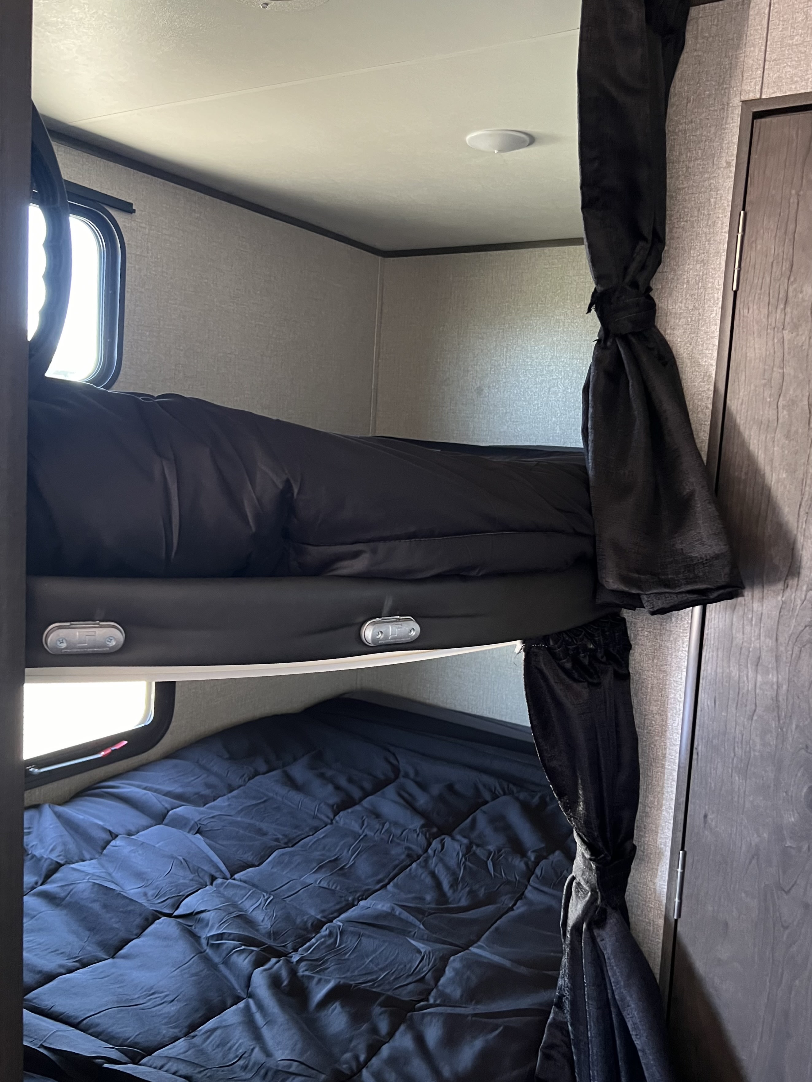 RV rental bunk beds with black comforters, windows, and privacy curtains, offering a cozy sleeping area.. Jayco Jay Flight SLX Rocky Mountain Edition 2020