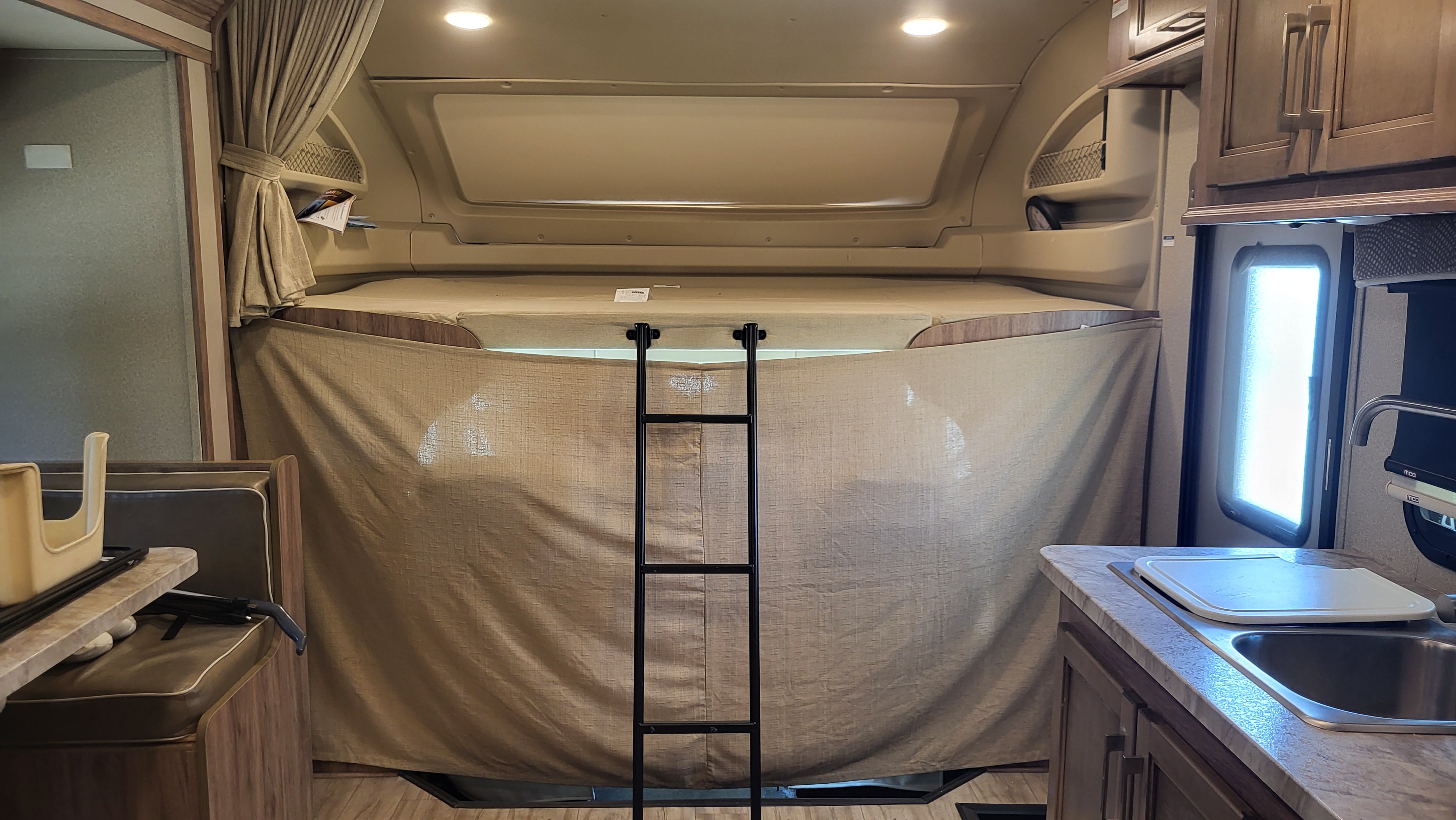Inside an rv rental, featuring a comfortable overhead bunk with ladder, kitchen counter with sink, and dinette seating for travelers.. Entegra Coach Odyssey 2019