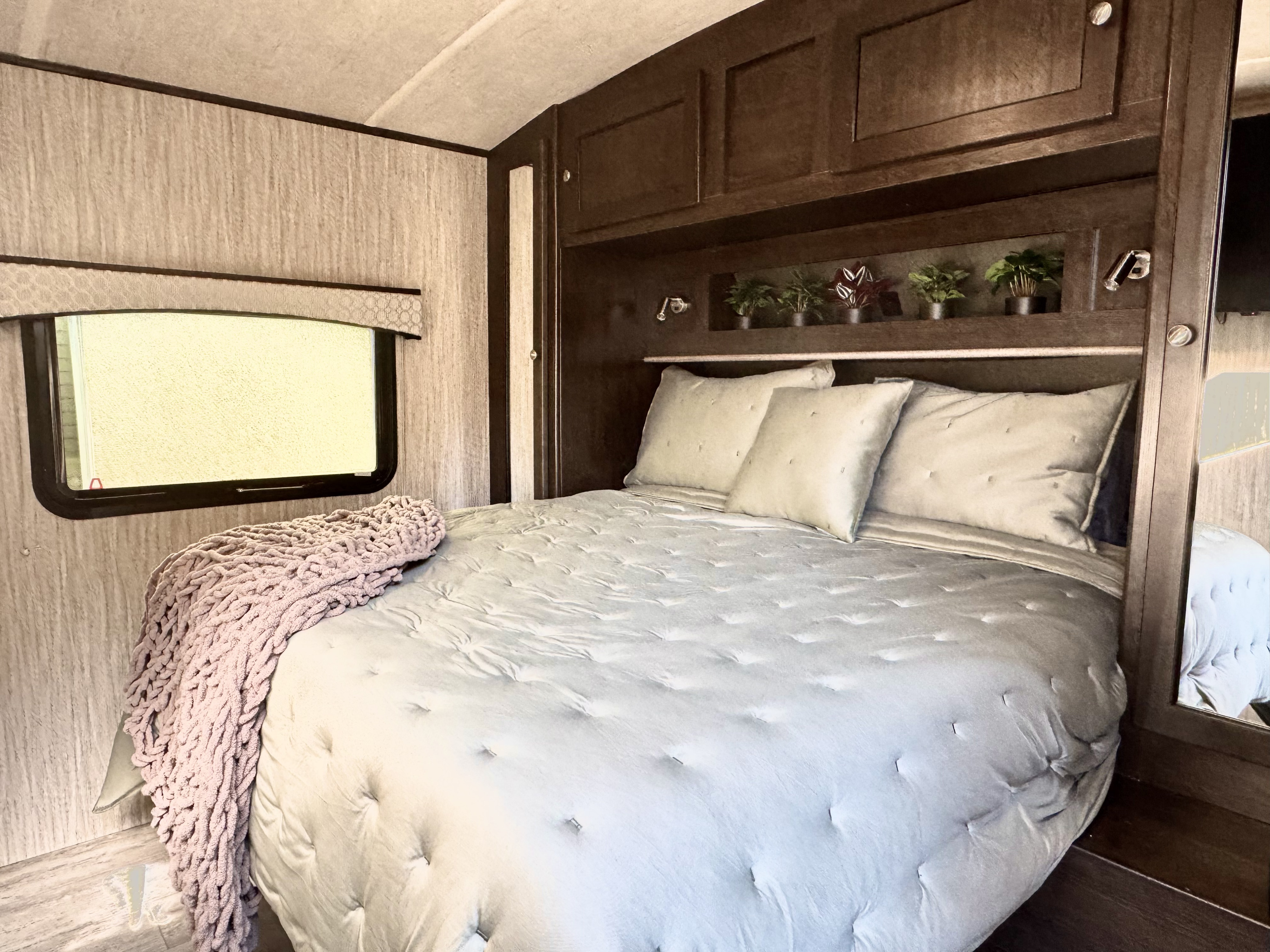 Cozy RV rental bedroom with comfortable light grey bedding, a pink throw, and dark wood overhead storage.. Cruiser RV Shadow Cruiser 2019