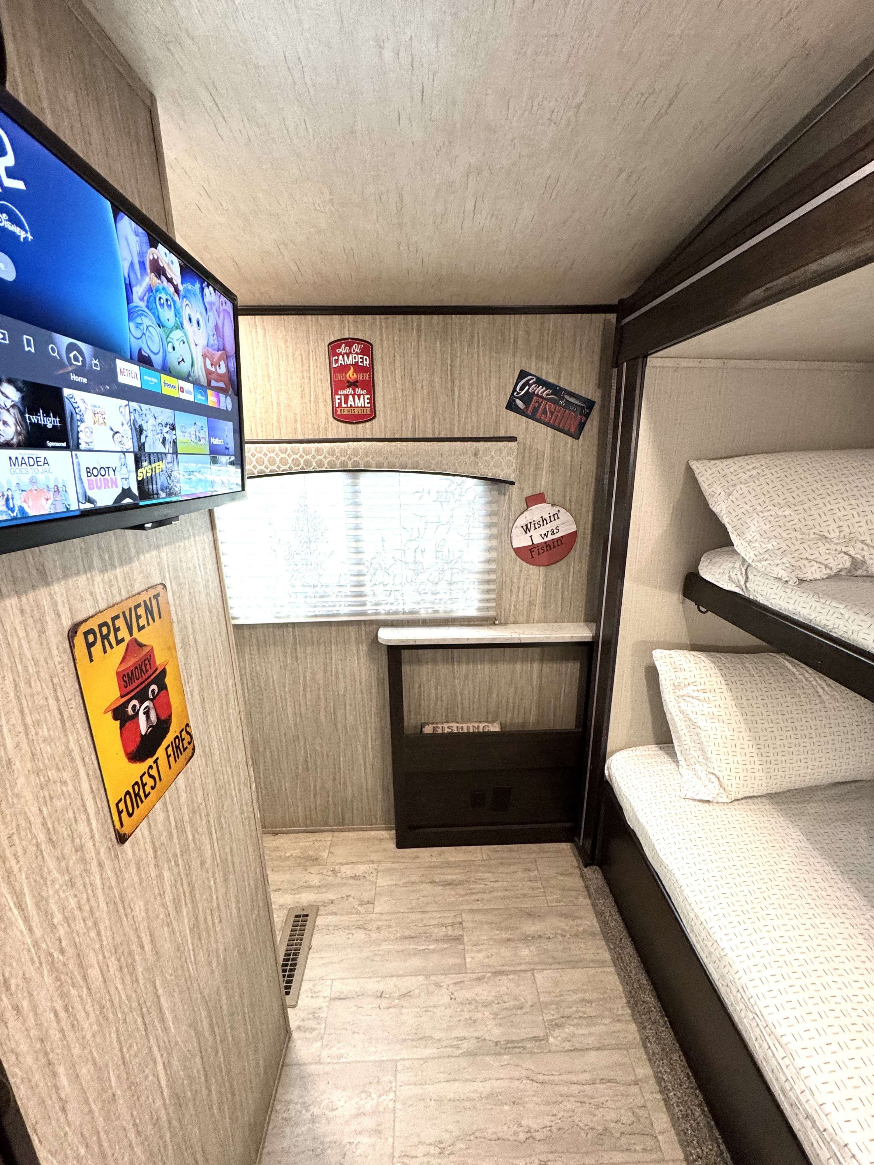 Cozy RV rental interior: TV & Smokey Bear sign on left wall, window with camping decor, bunk beds on right. Tiled floor.. Cruiser RV Shadow Cruiser 2019